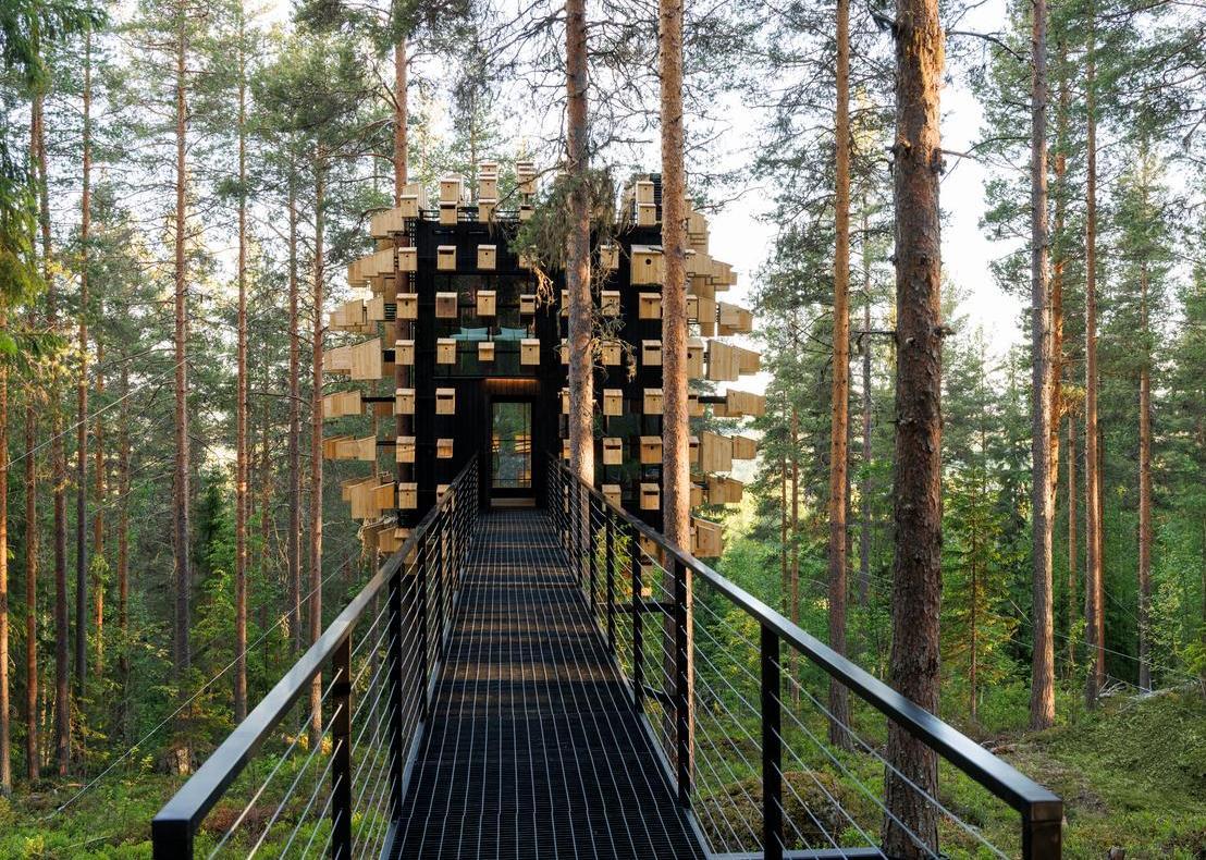 Looking down a long metal walkway toward a spherical structure covered in wooden birdhouses.