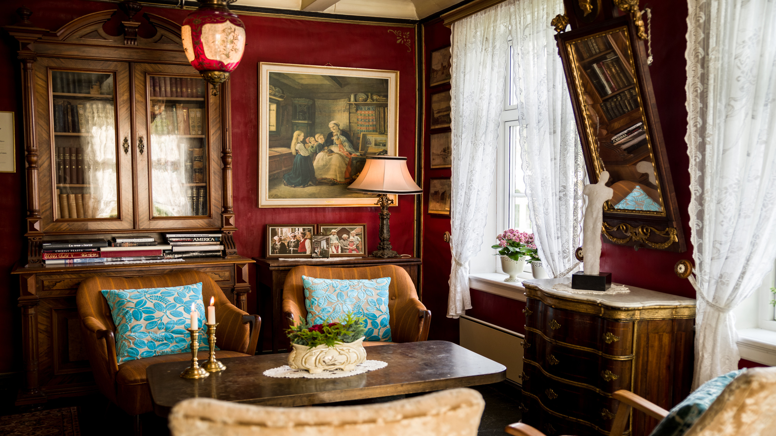 Elegant vintage room with rich red walls, ornate furniture, and lace curtains.