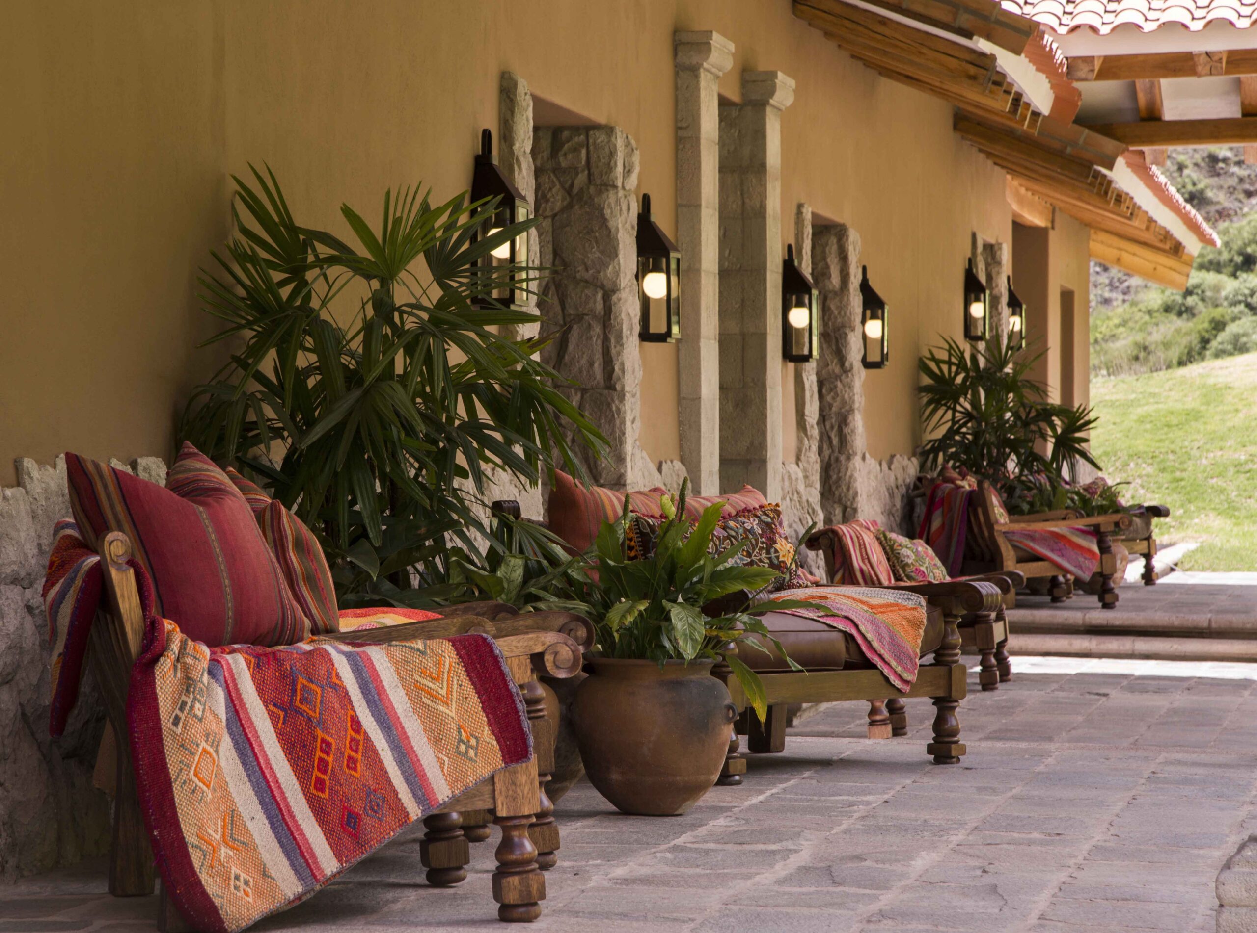 Rustic outdoor seating area with wooden benches adorned with colorful textiles and plants.