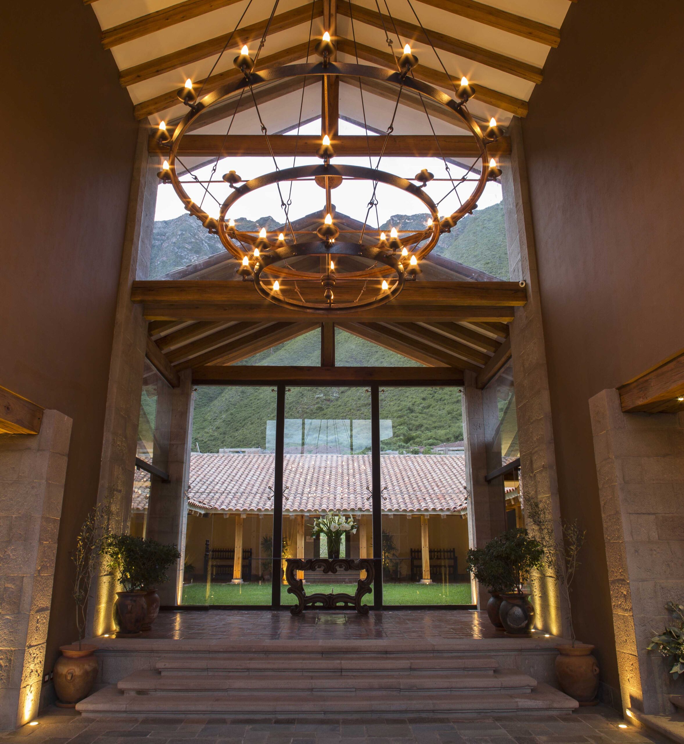 Elegant indoor space with a circular chandelier, overlooking a courtyard and mountains.