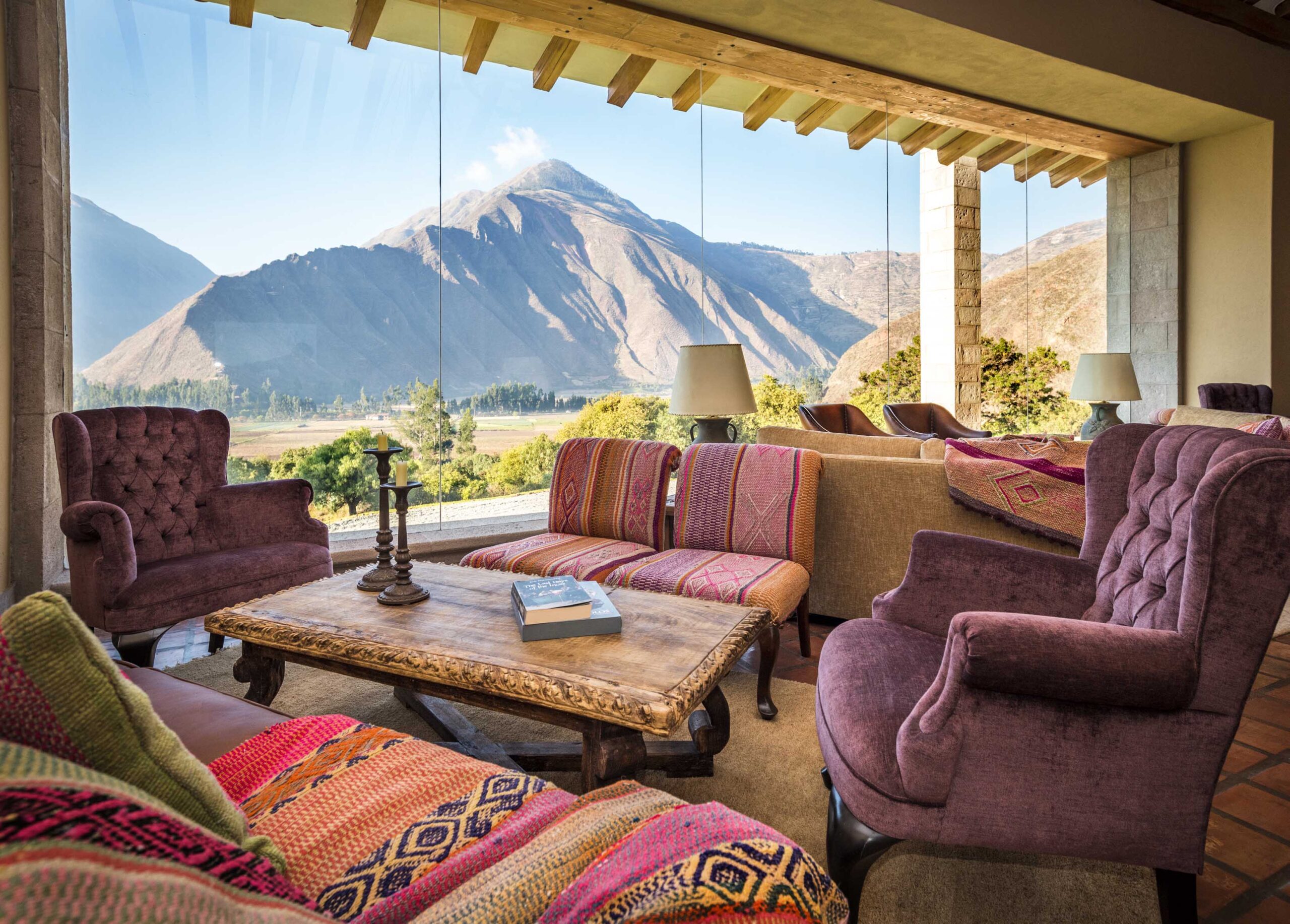 Cozy room with plush chairs, patterned cushions, rustic table, and a mountain view through a large window.
