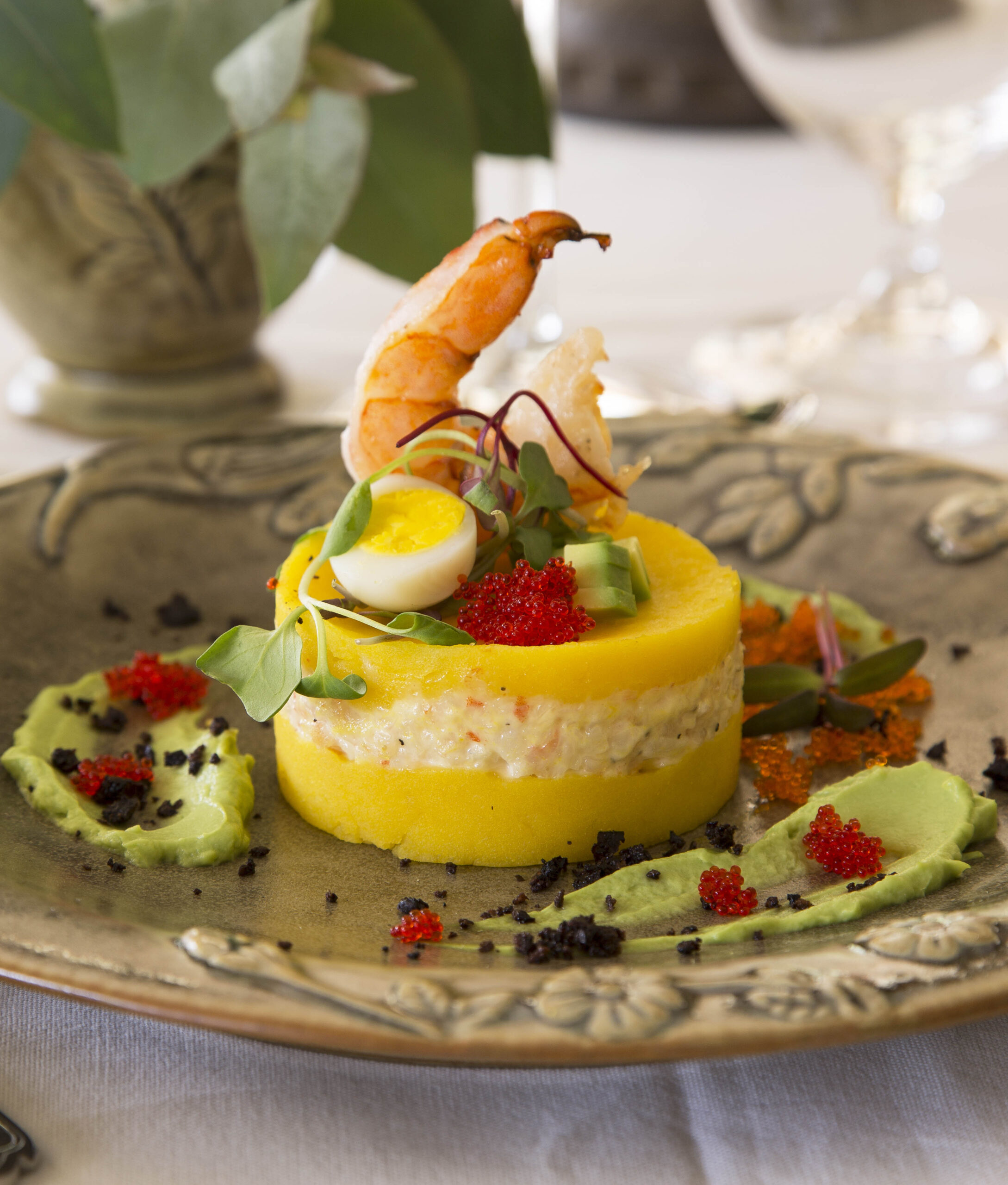 A gourmet dish with layers of yellow polenta, crab salad, shrimp, roe, and a quail egg.