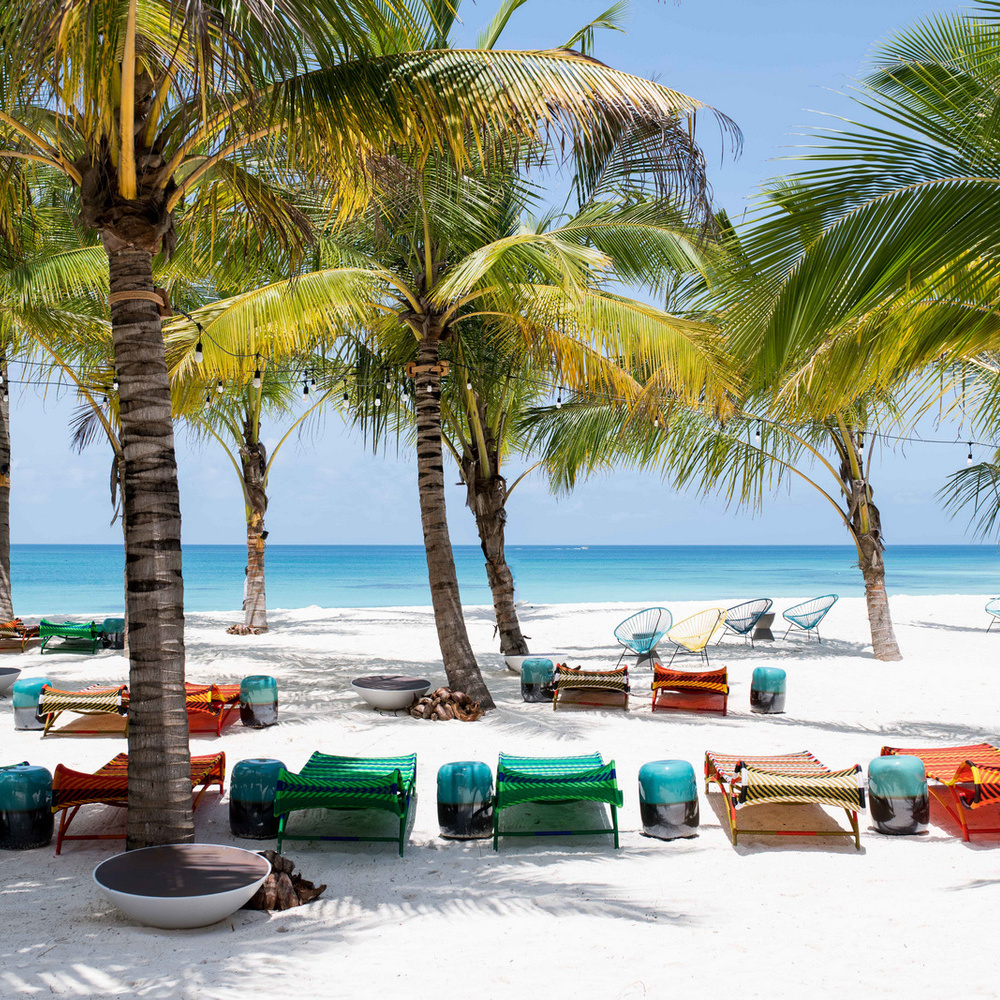 Vibrant green and orange beach loungers under palm trees on a white sand beach at Zuri Zanzibar.