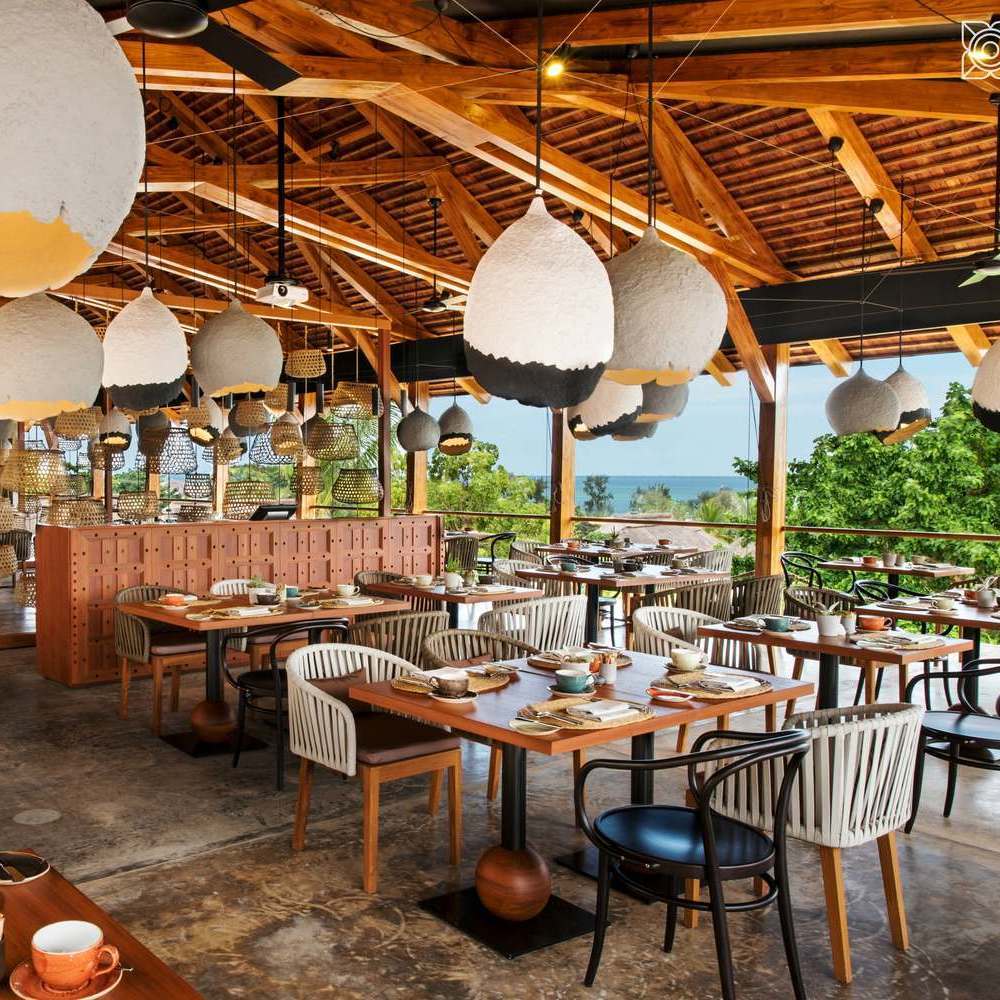 Indoor-outdoor restaurant with wooden beams, unique white and black pendant lamps, and ocean views at Zuri Zanzibar.