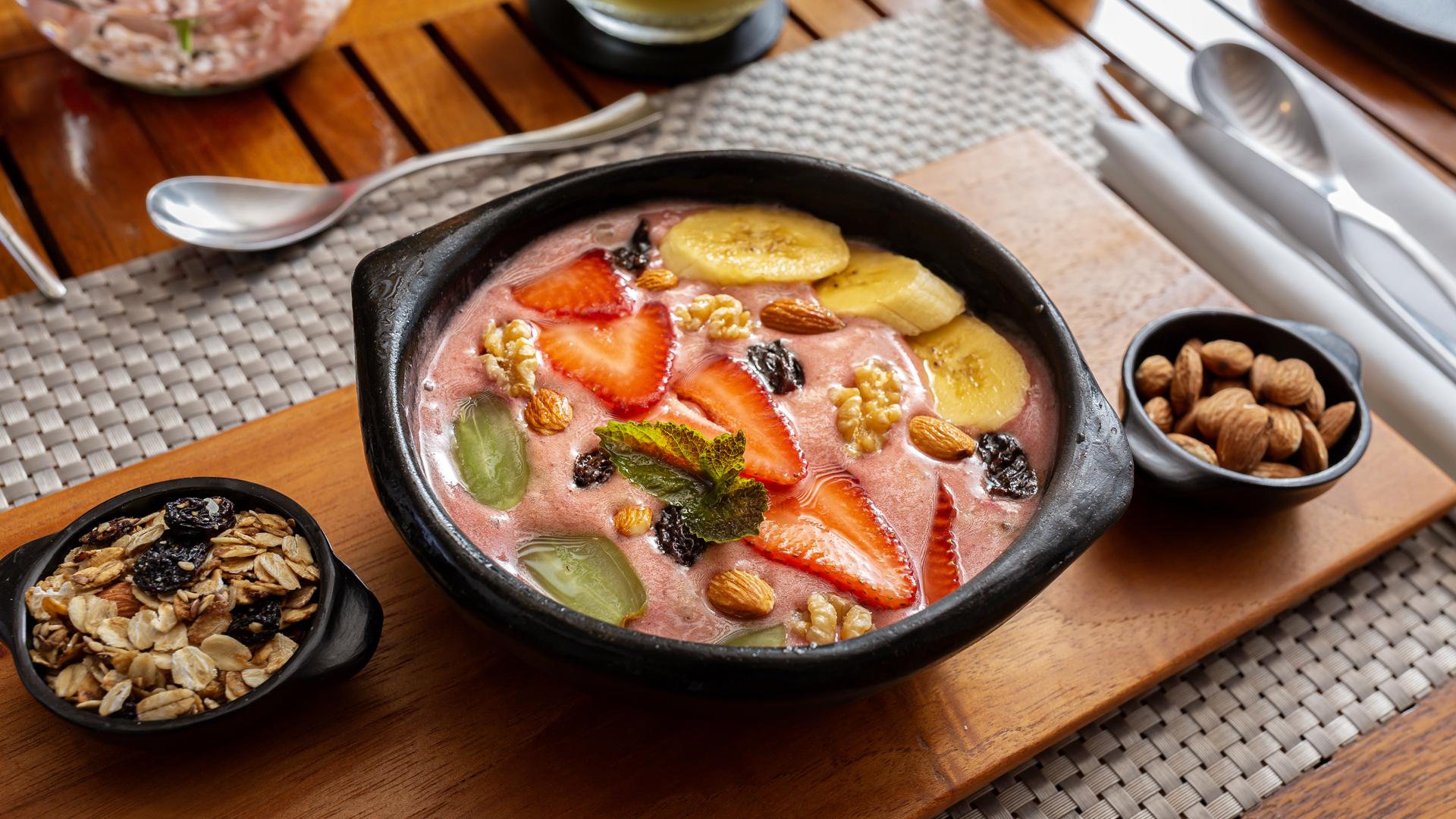 A bowl of acai smoothie topped with sliced fruits, nuts, and granola on a wooden table.