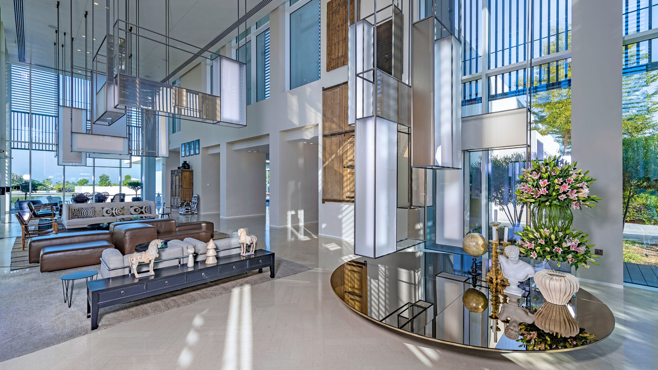 Large modern hotel lobby with tall glass walls, brown leather seating, and unique rectangular hanging lanterns.