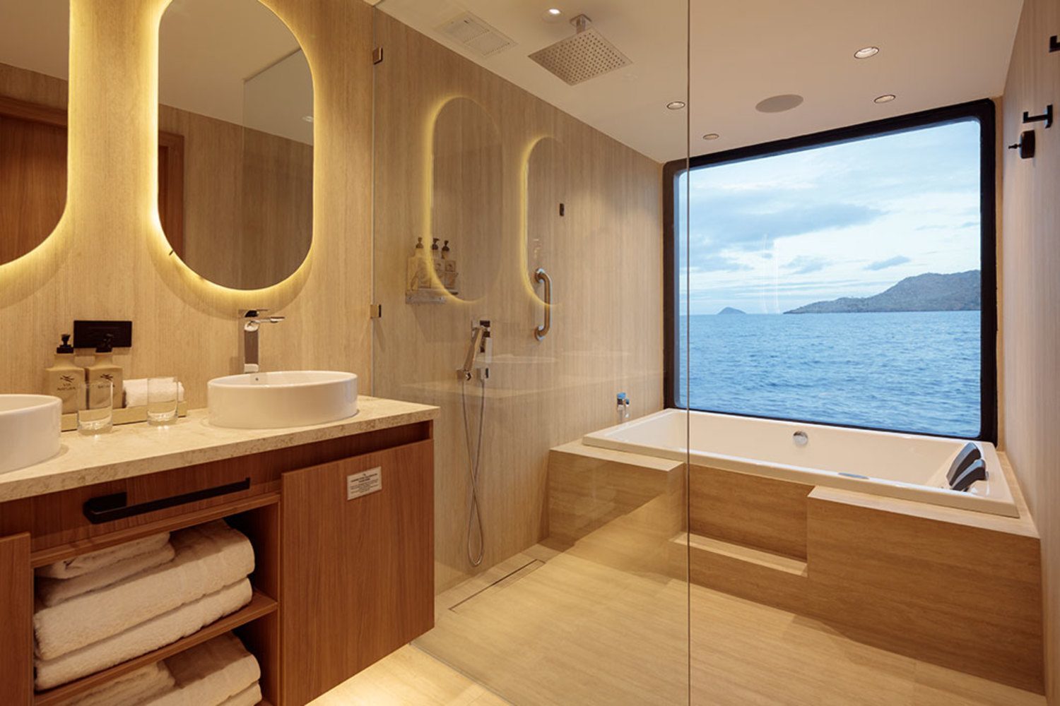 Modern catamaran bathroom featuring a double vanity, glass shower, and bathtub beside a large ocean-view window.