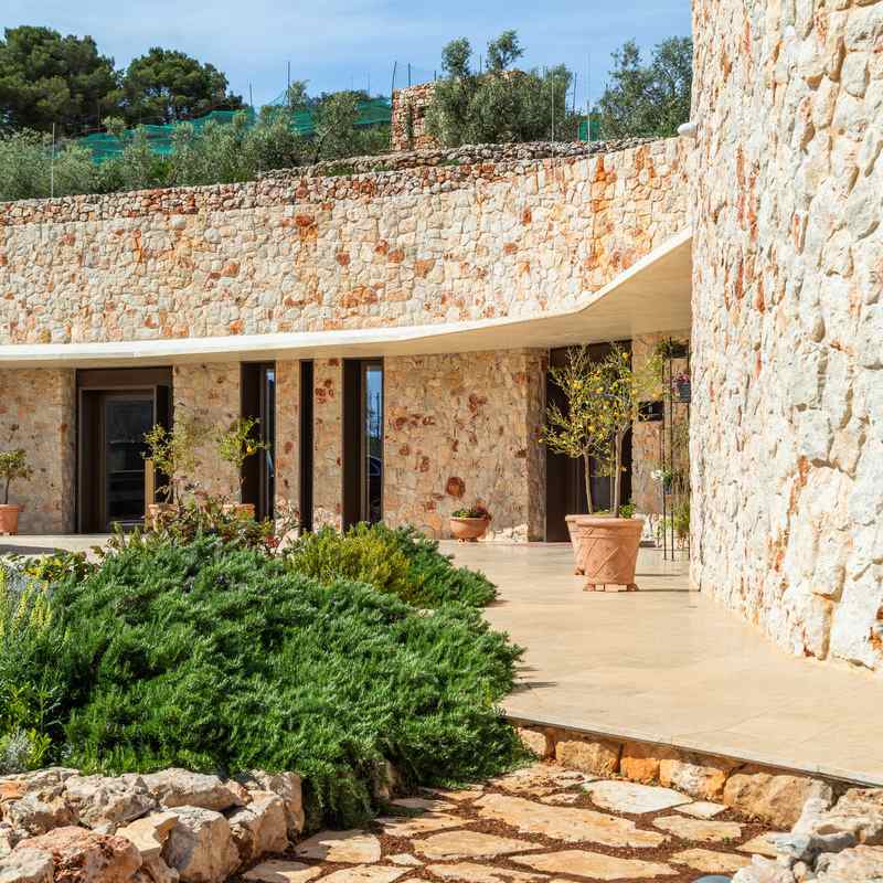The exterior of Villa Nai 3.3 featuring a long, curved wall made of light-colored natural stone.
