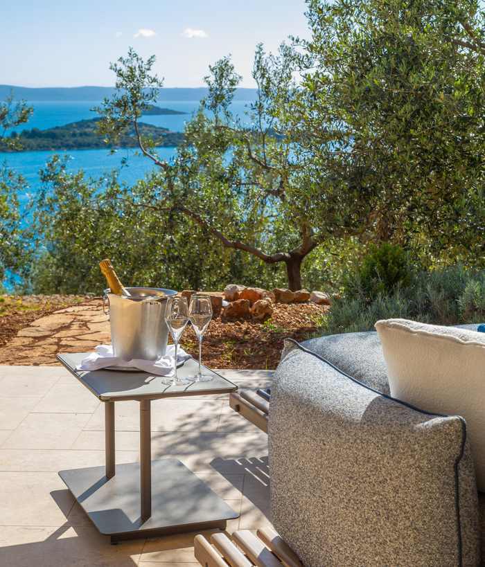 Champagne in an ice bucket on a small table by an outdoor sofa with a scenic view of the sea.