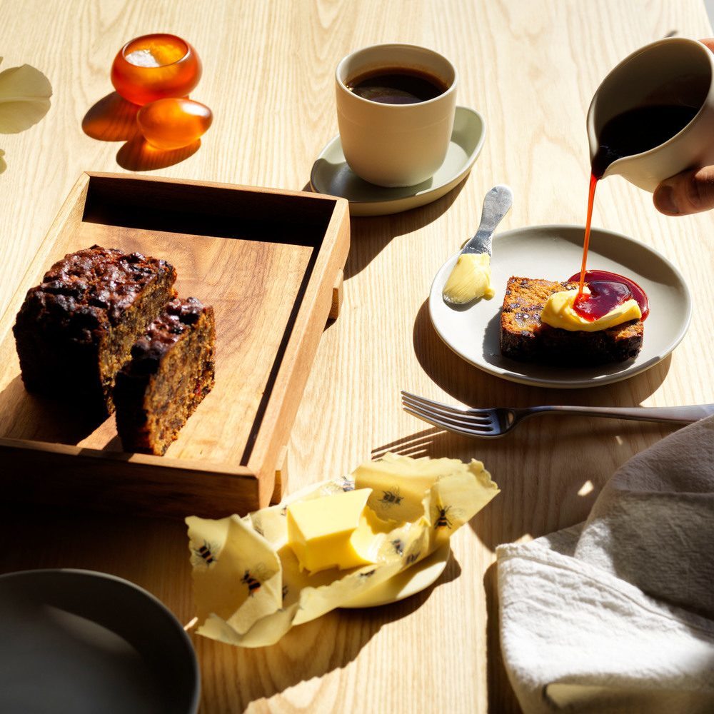 Sliced loaf cake on a tray with butter, coffee, and sauce pouring onto a slice.