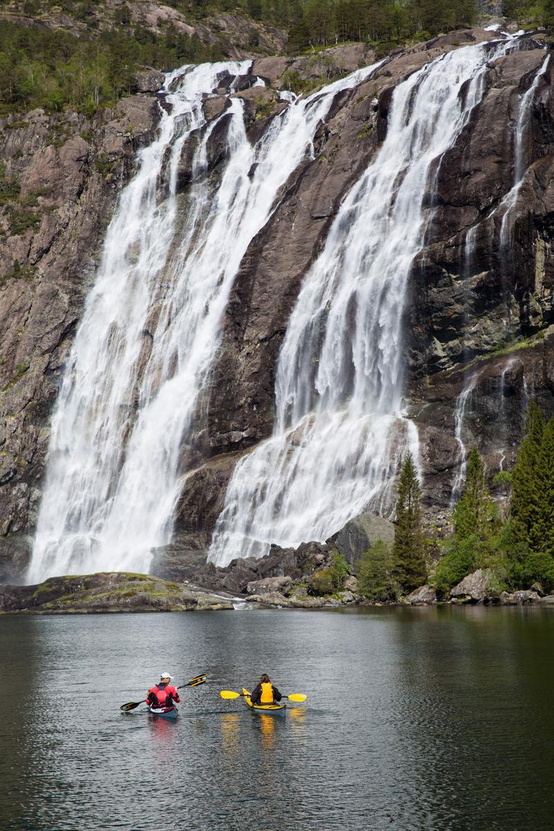Two people on canoes at the base of a waterfall.