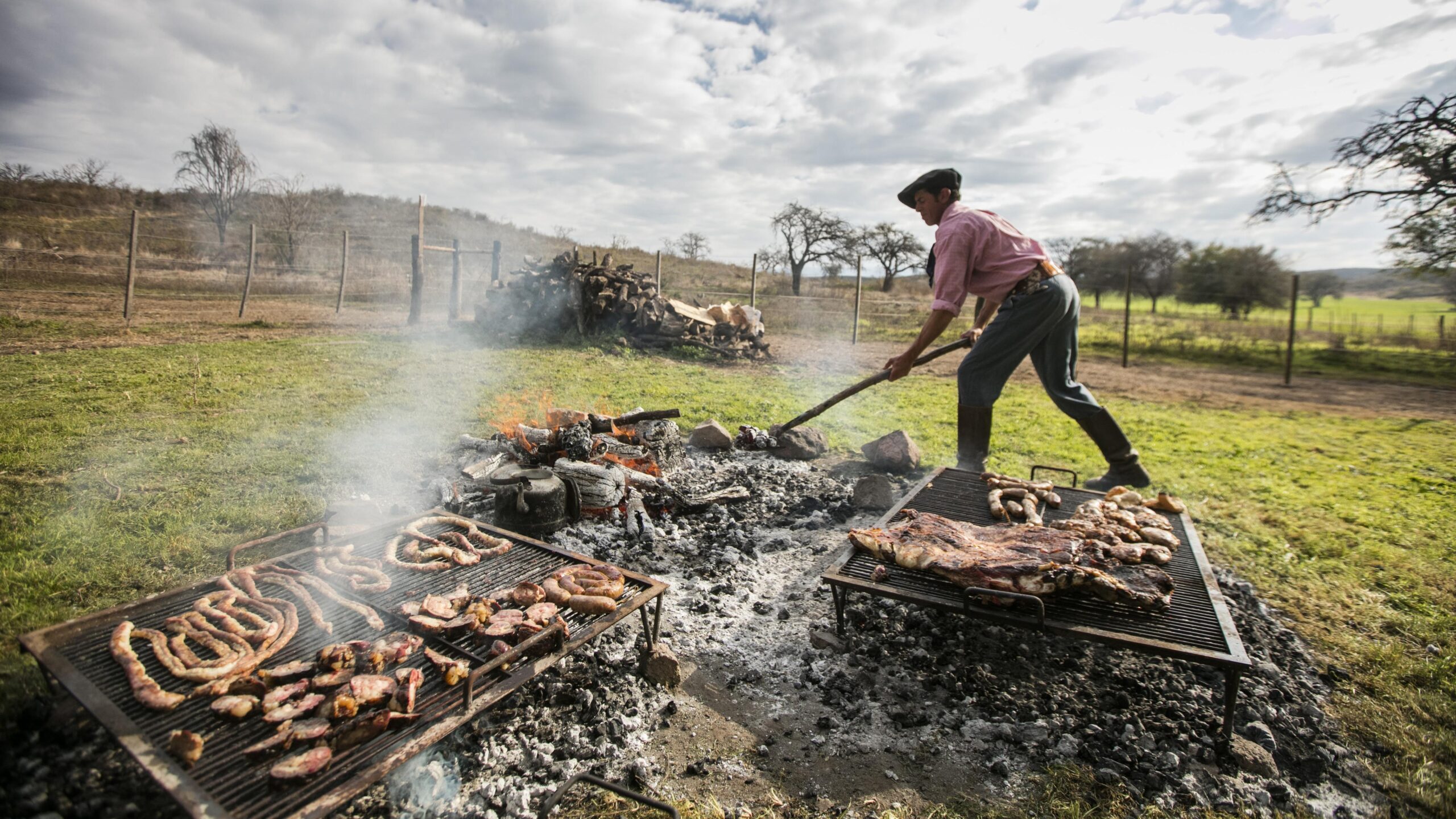 Person grilling various meats outdoors on a sunny day.