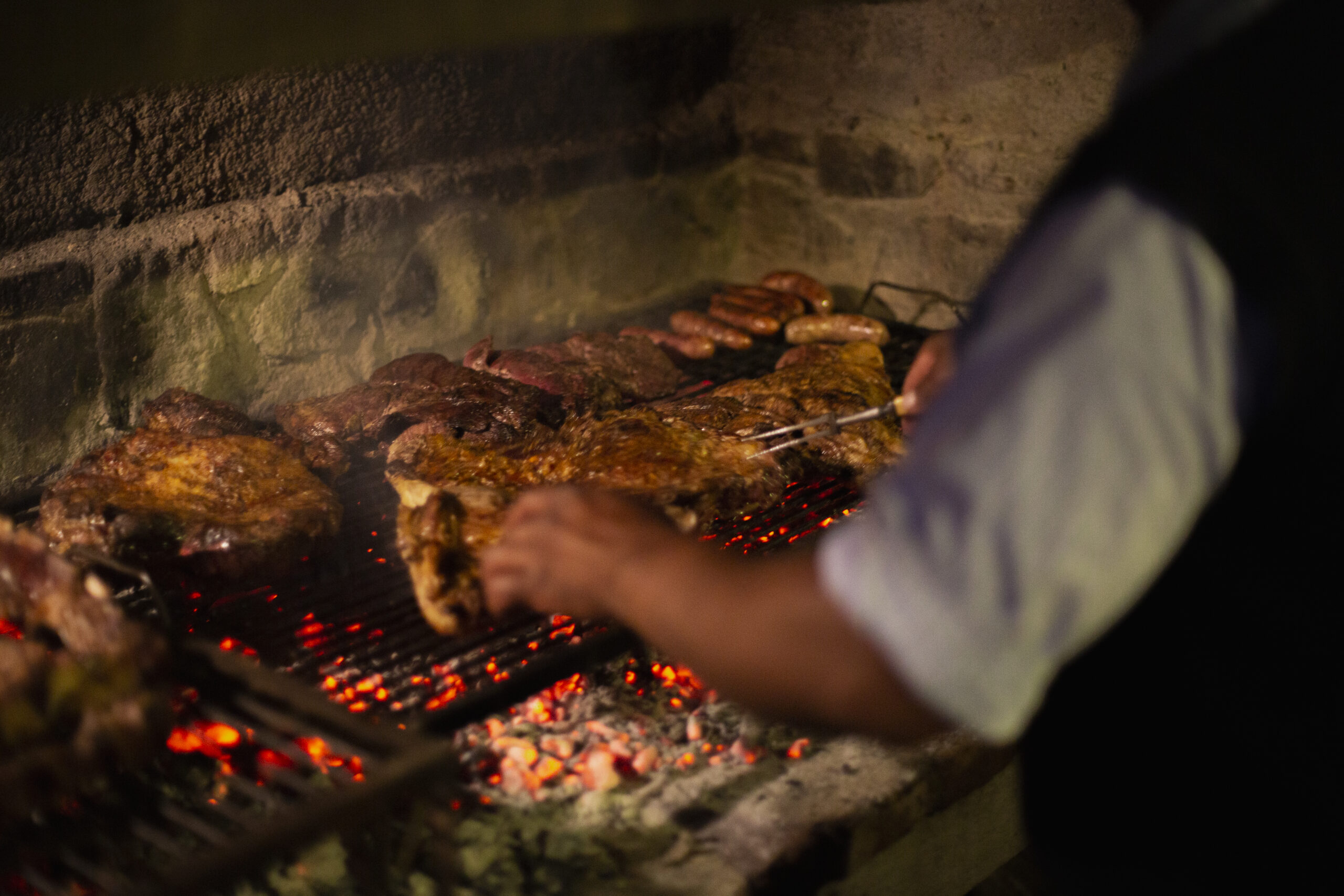 Person grilling various meats over a charcoal barbecue.
