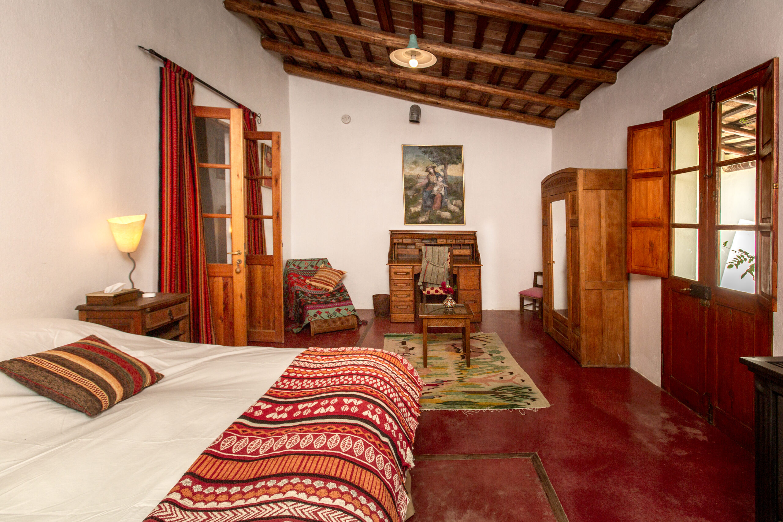 Rustic bedroom with a patterned bedspread, wooden furniture, and beamed ceiling.