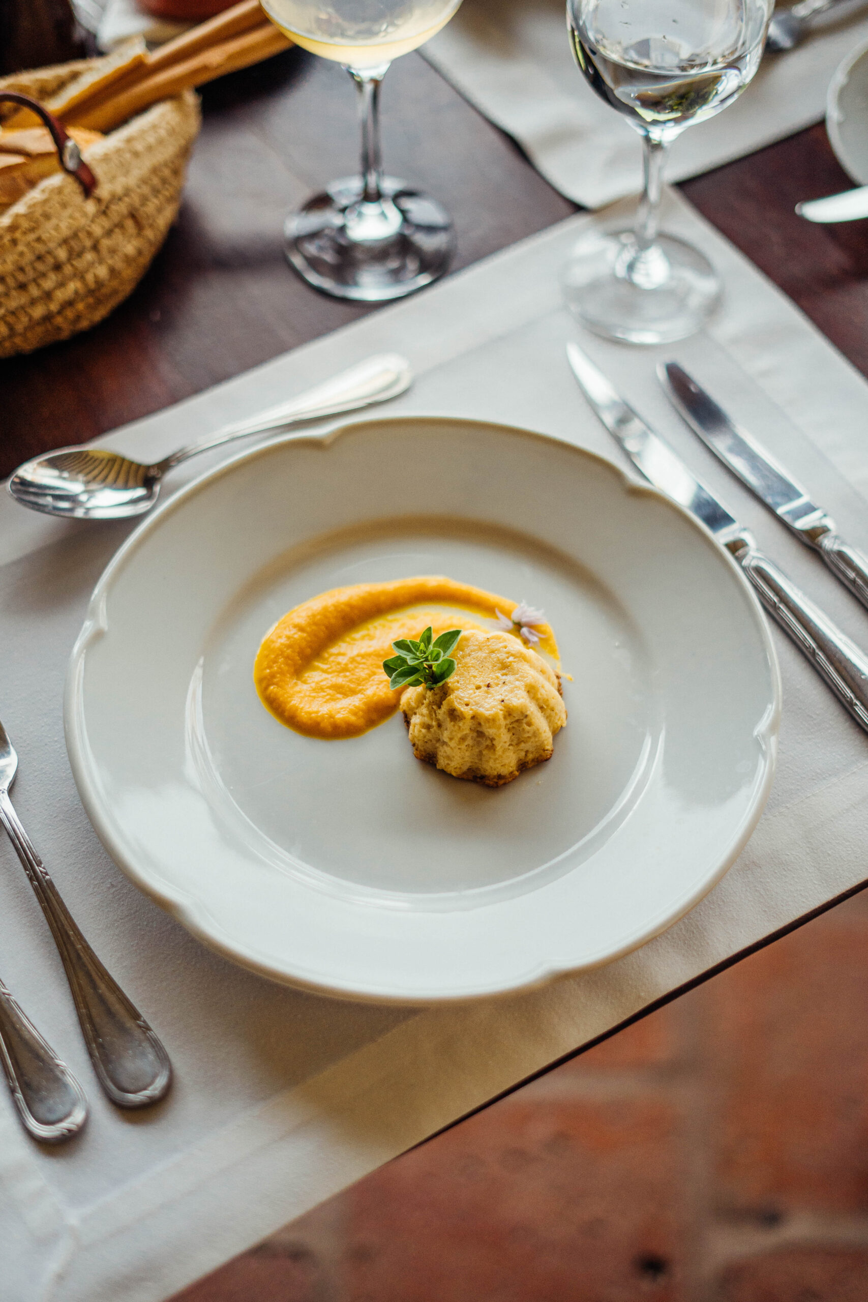 Elegant dining setup with a gourmet dish served on a white plate, wine glasses, and cutlery on a wooden table.
