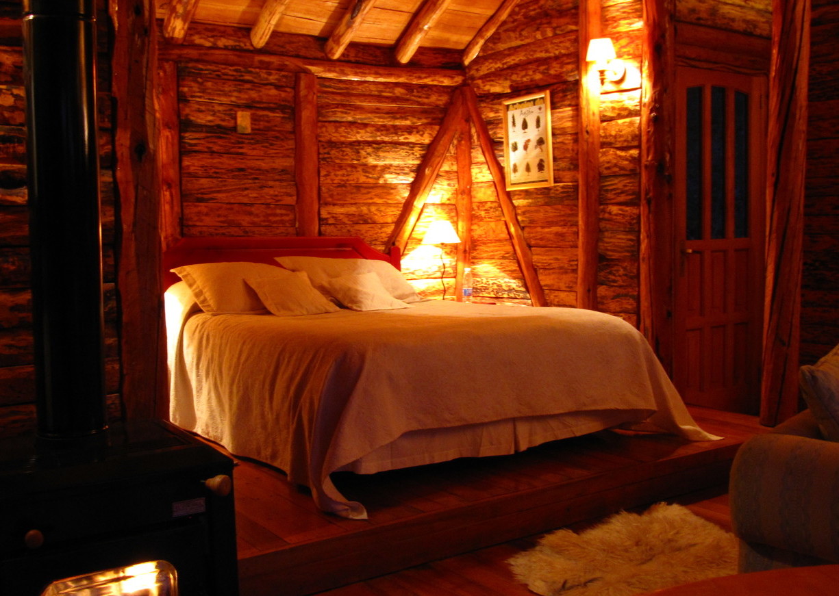 A bedroom in a log cabin lit up by lamps at Mallín Colorado, Chile
