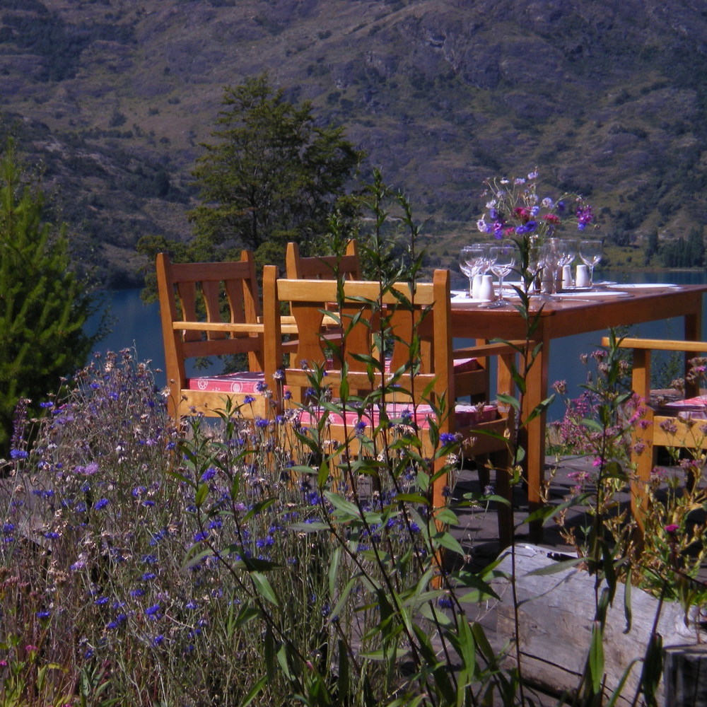 A wooden table and chairs sat by a lake, surrounded by flowers at Mallín Colorado, Chile