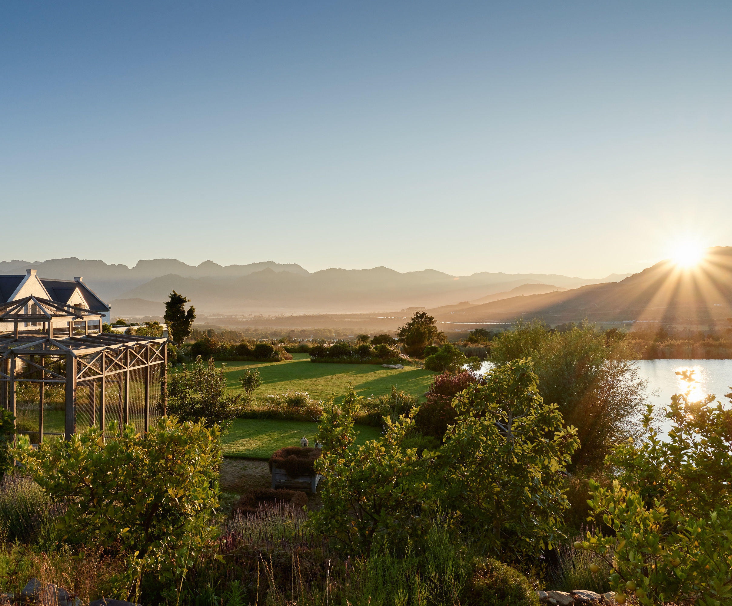 Sunrise over a serene landscape with mountains, a gazebo, and a lake.