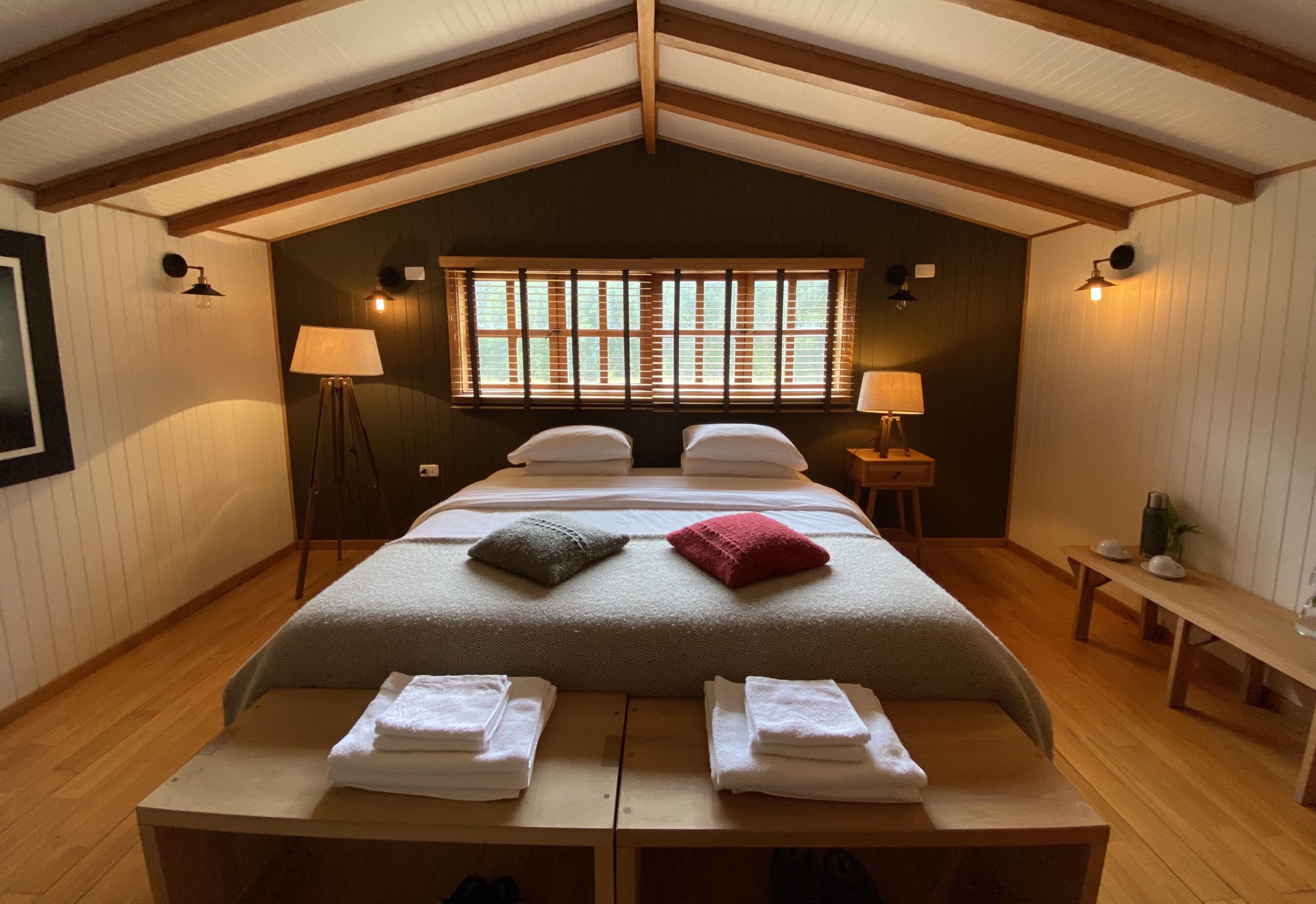 Cozy bedroom with a large bed, wooden accents, warm lighting, and two windows.