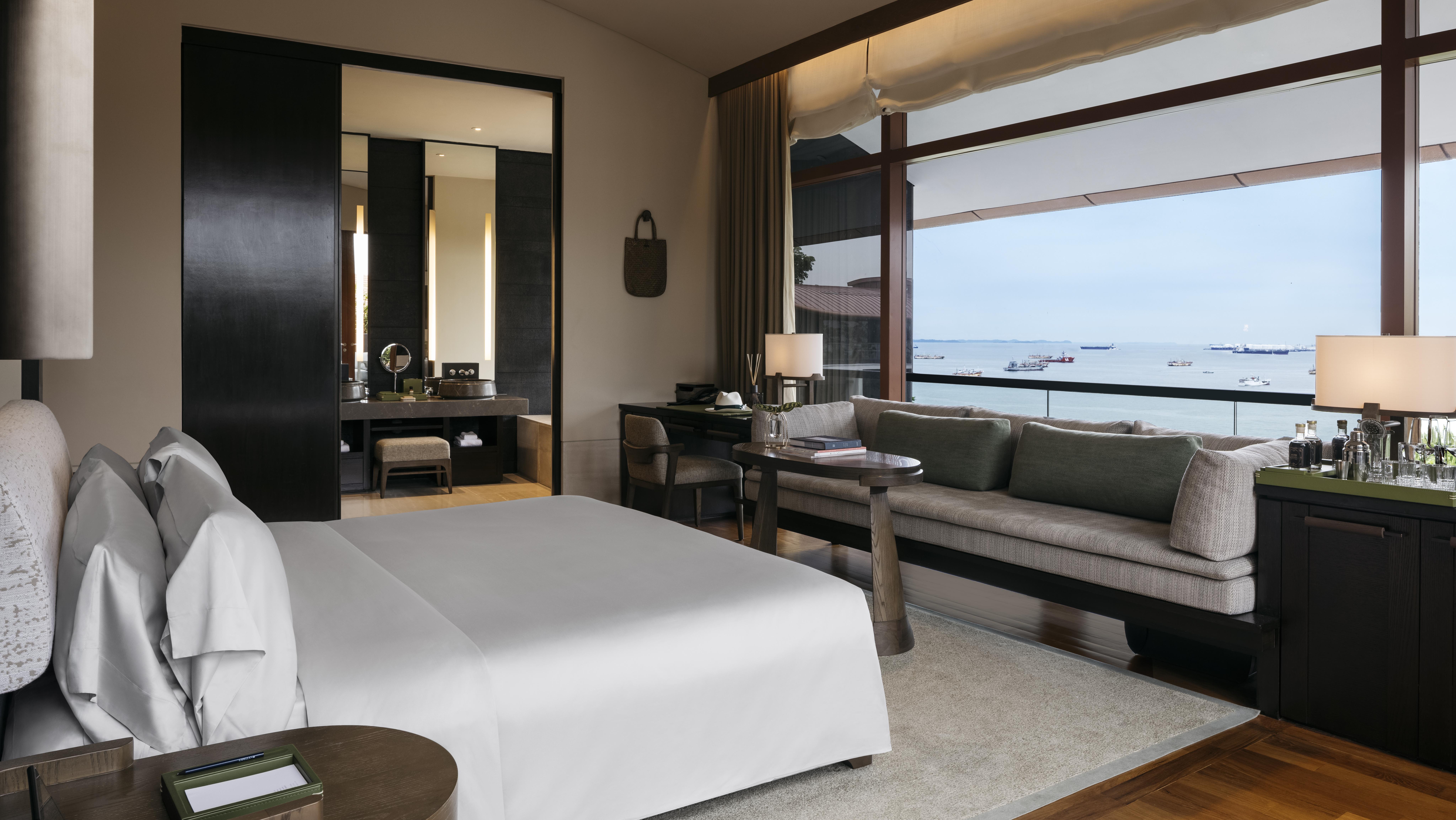 Luxury hotel room with bed, seating area, and large window overlooking the sea with ships.