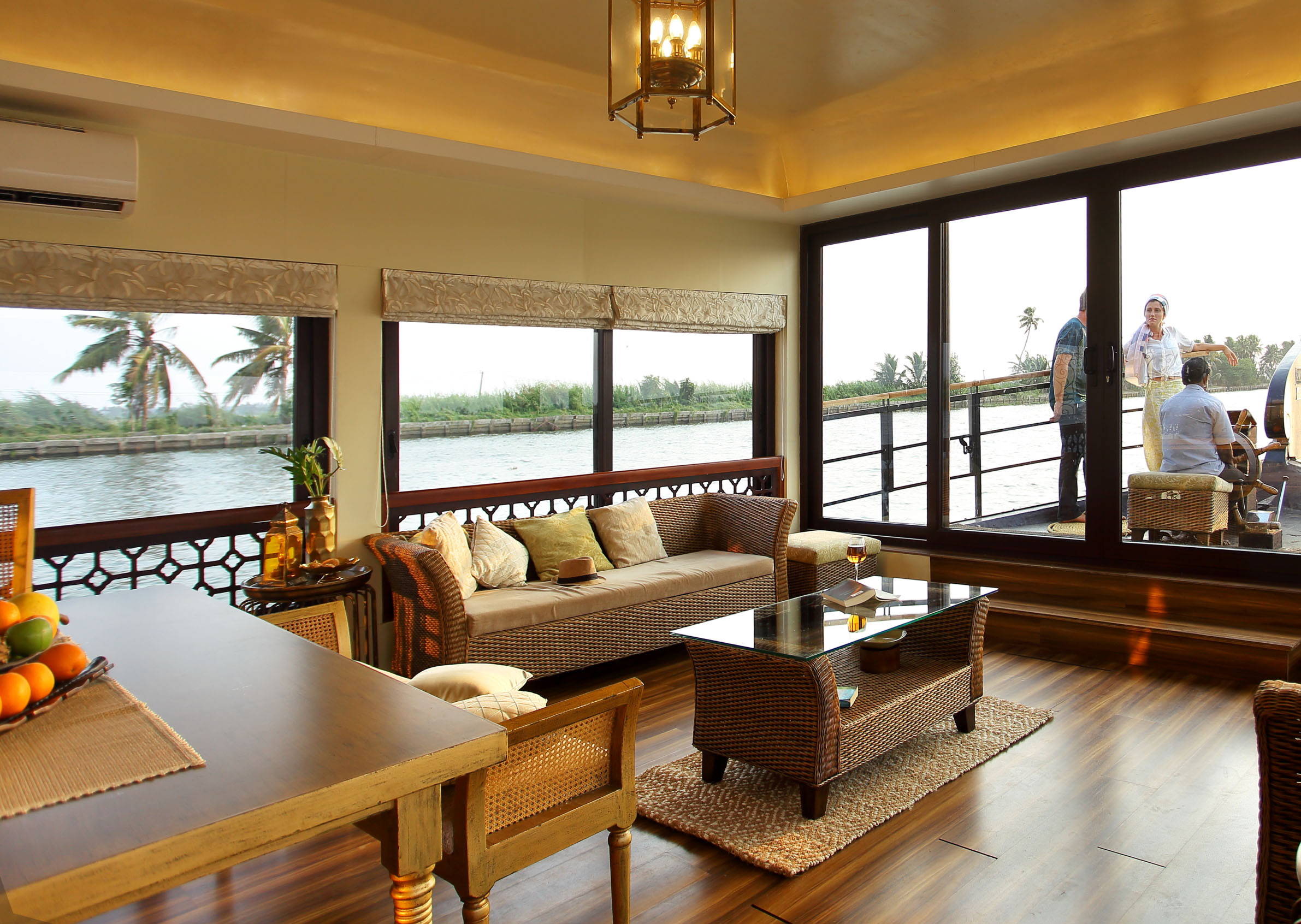 A cozy living room with wicker furniture overlooking a riverside balcony.