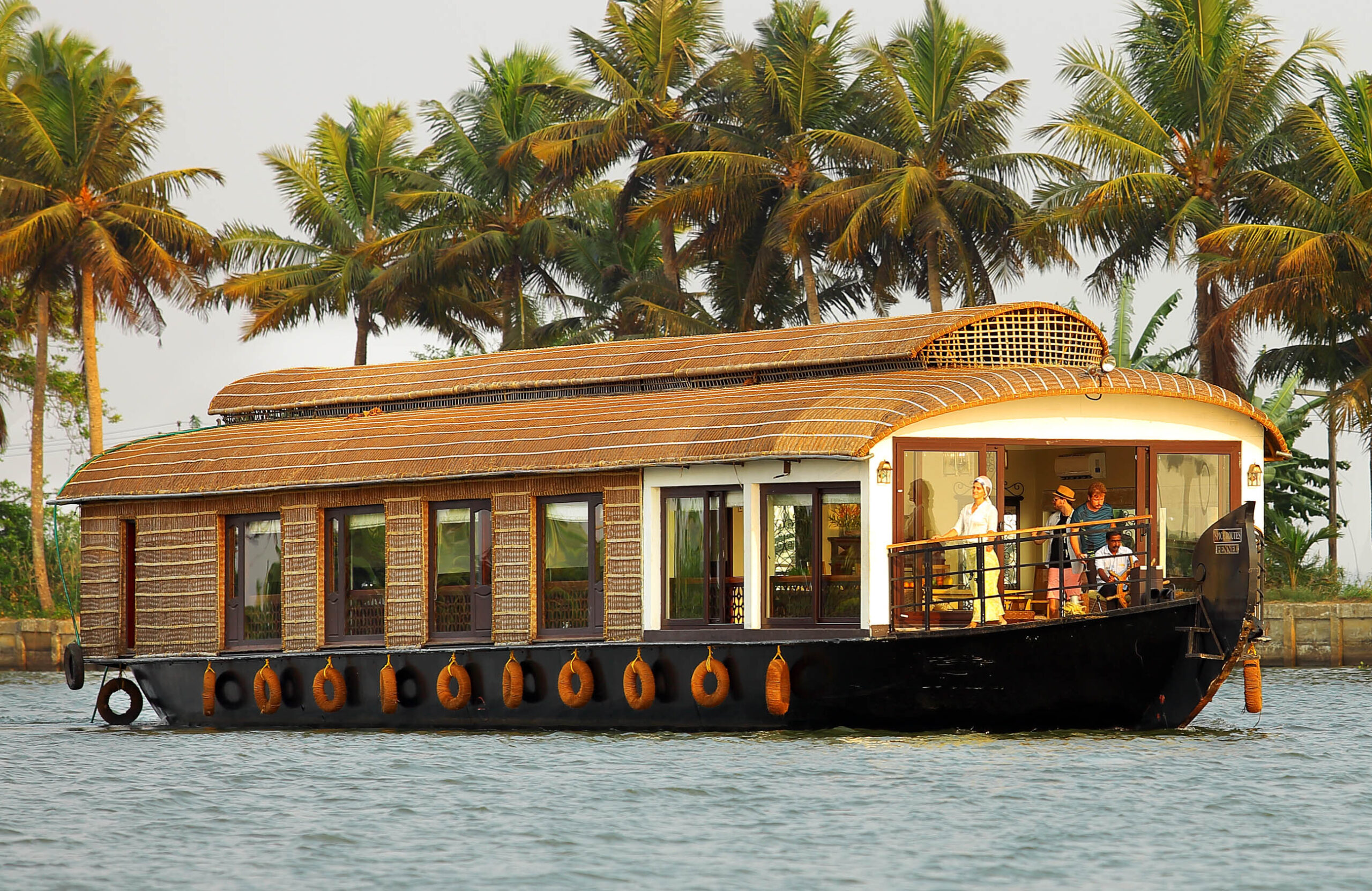 Traditional houseboat floating on river with palm trees in the background.
