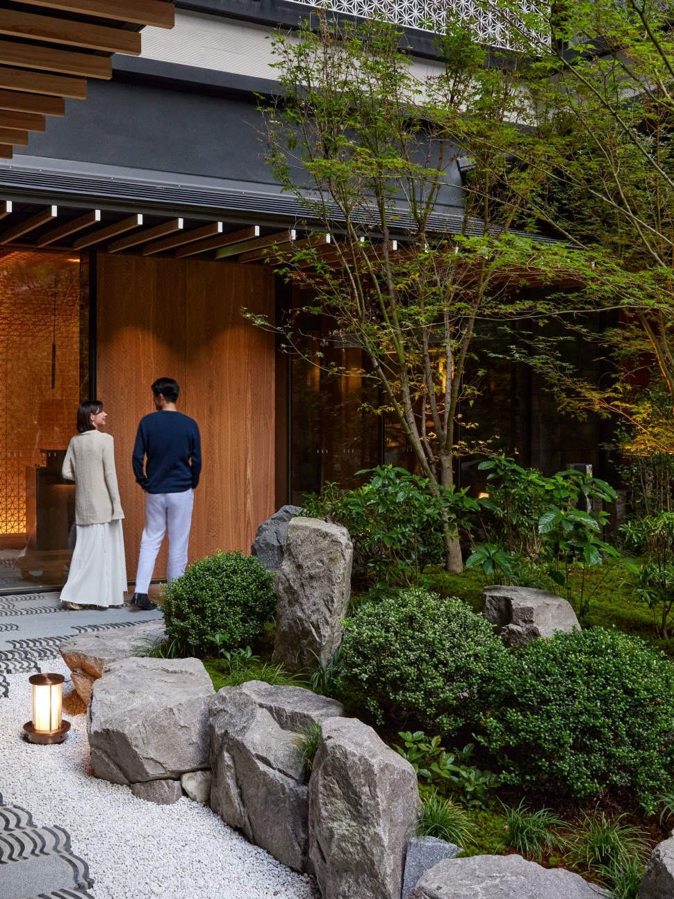 Two people at the entrance of a building with a Japanese-style garden and lantern.