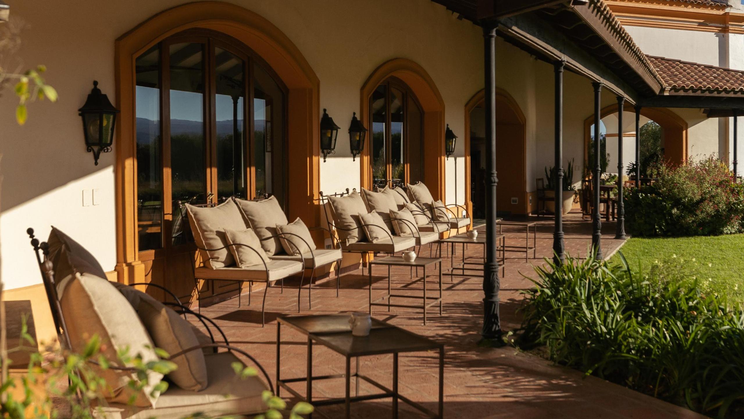 Elegant patio with cushioned chairs aligned along arched windows of a stucco building.