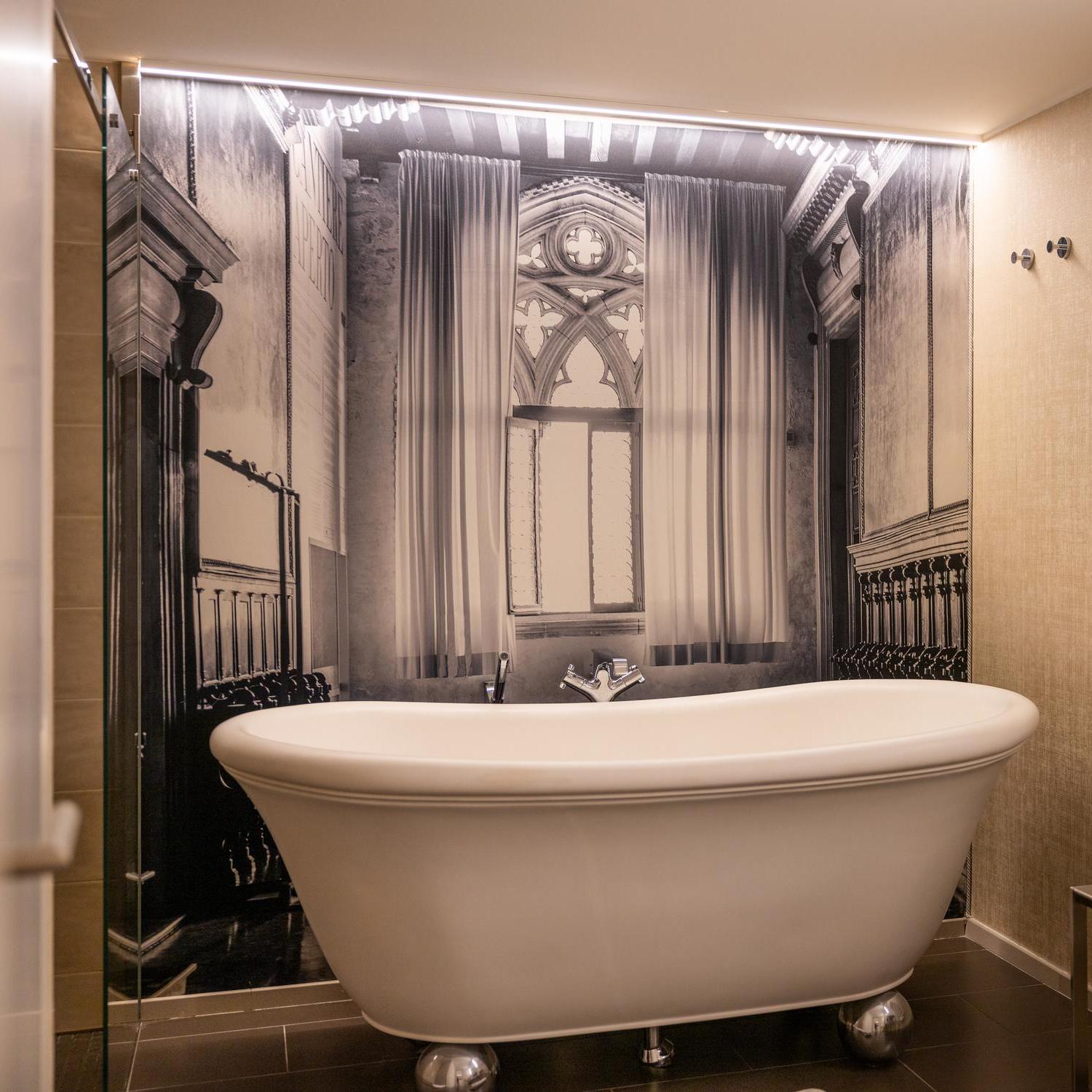 A vintage-style freestanding bathtub in a bathroom with a monochrome architectural mural.