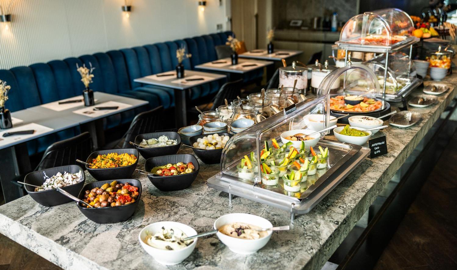 Elegant buffet setup with assorted dishes and salad bar in a restaurant with blue seating.