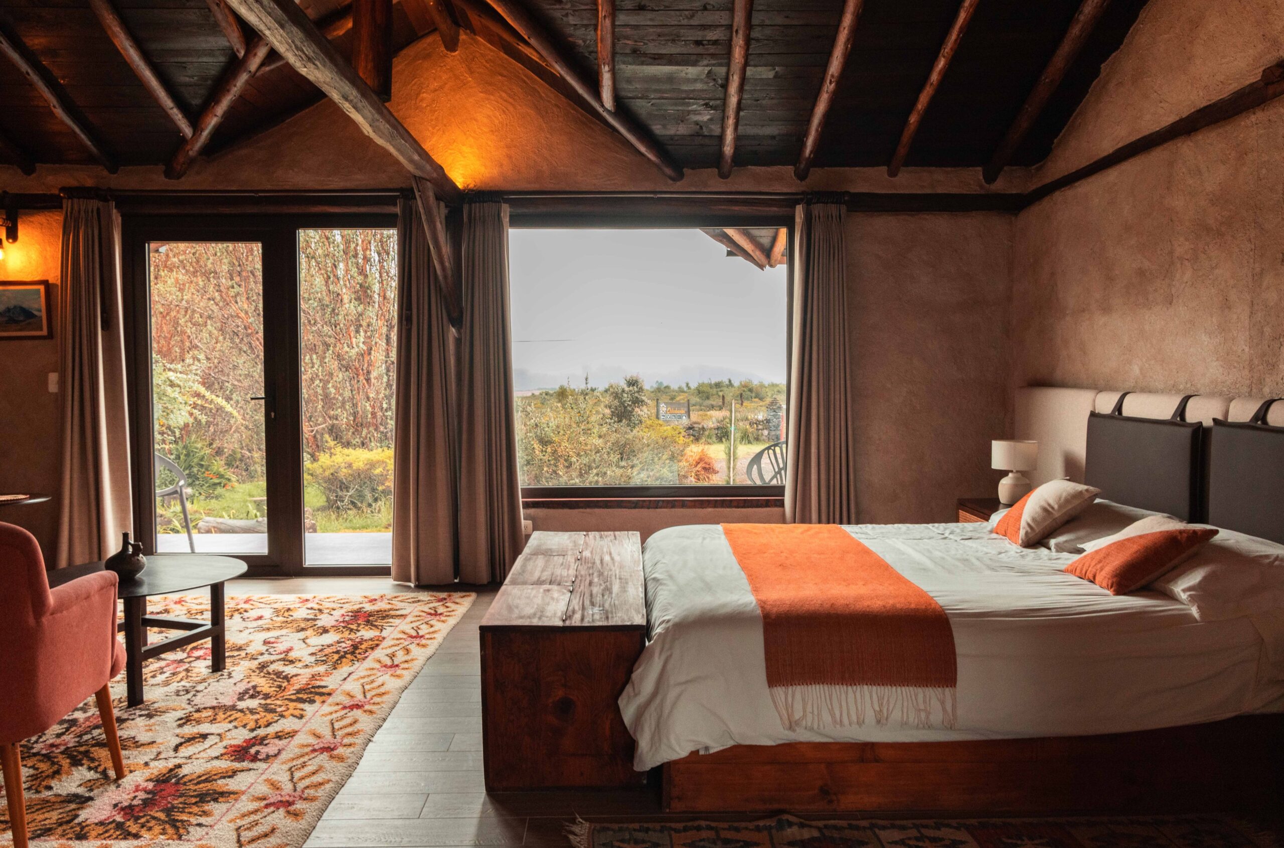 Cozy bedroom with rustic decor and view of autumn landscape through glass doors.