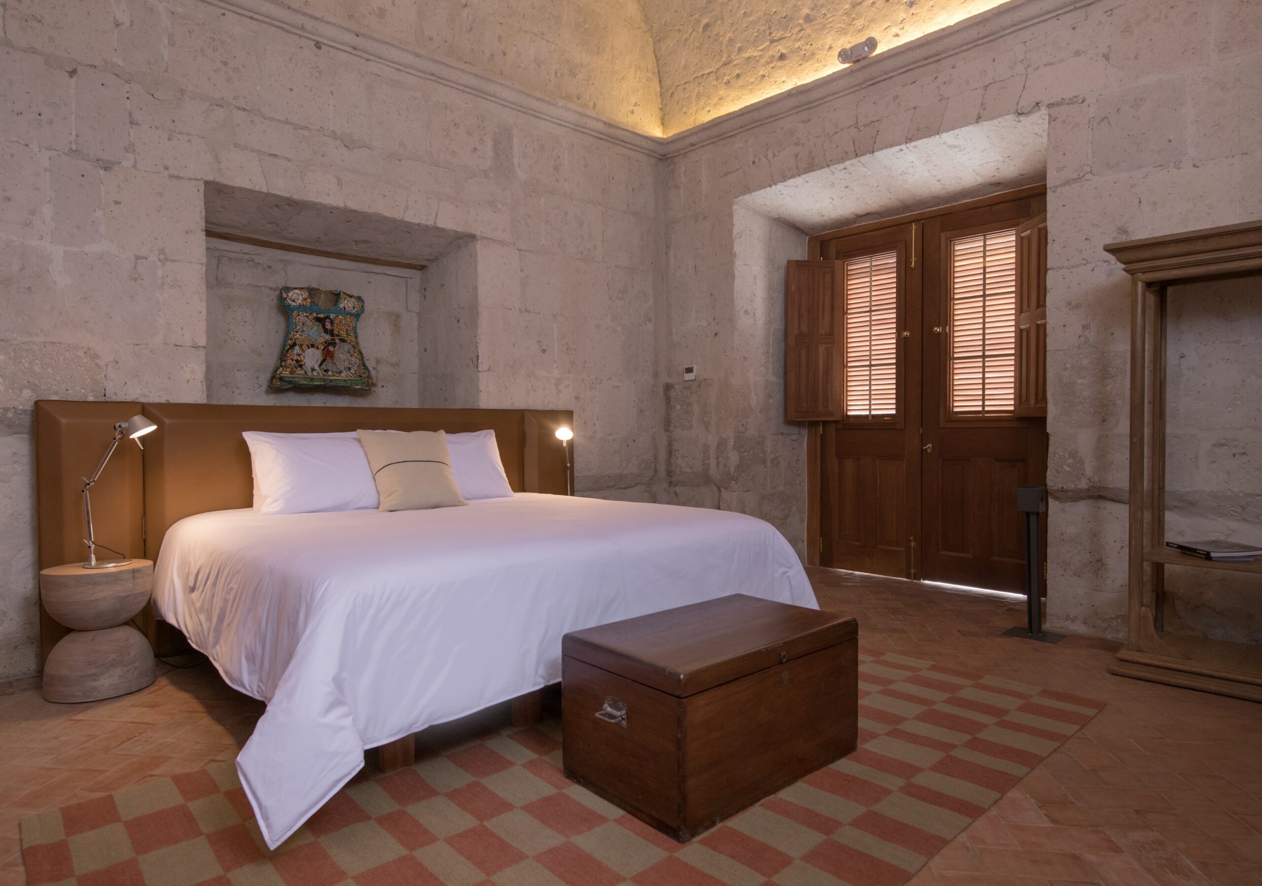 Elegant bedroom with a large bed, stone walls, checkered floor, and wooden shutters.