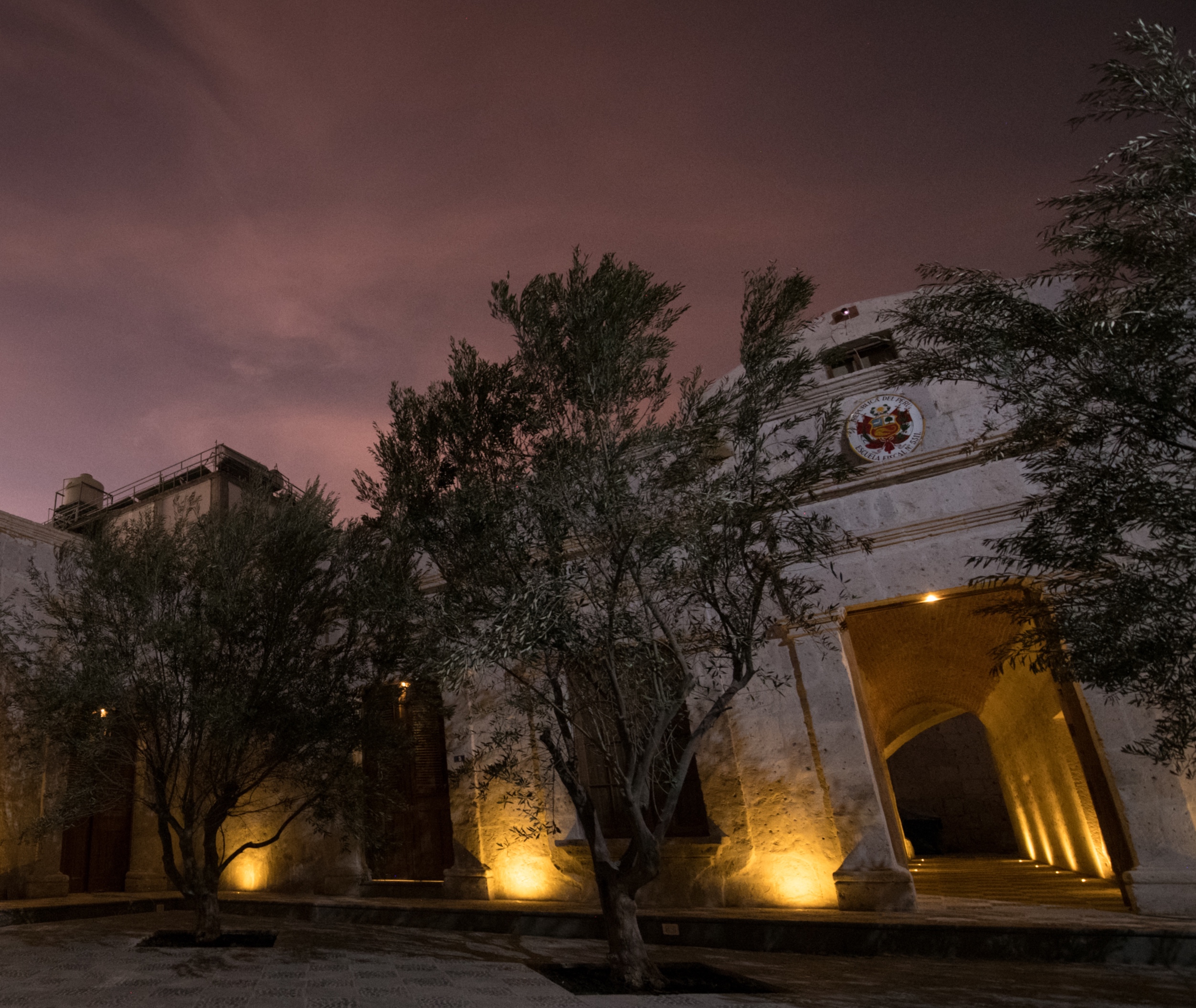 Colonial building with illuminated archway and trees under a twilight sky.