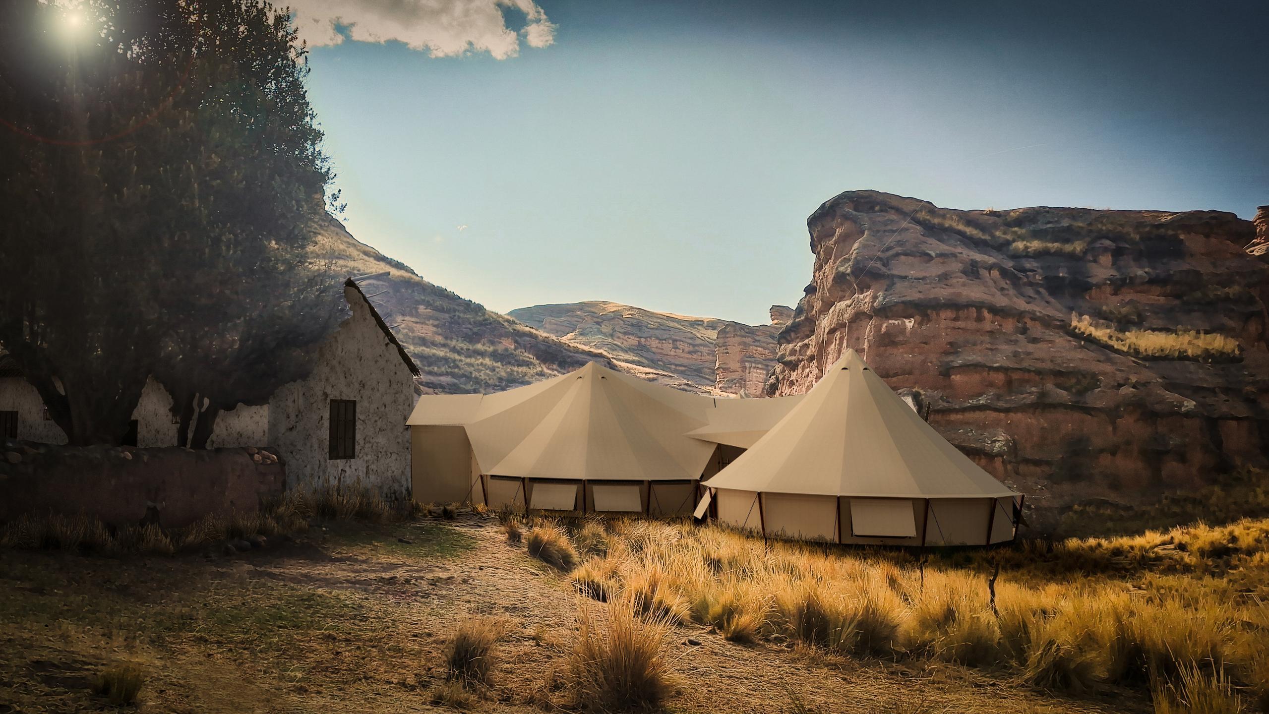 Luxury canvas tents in a field with a backdrop of cliffs and a clear sky.