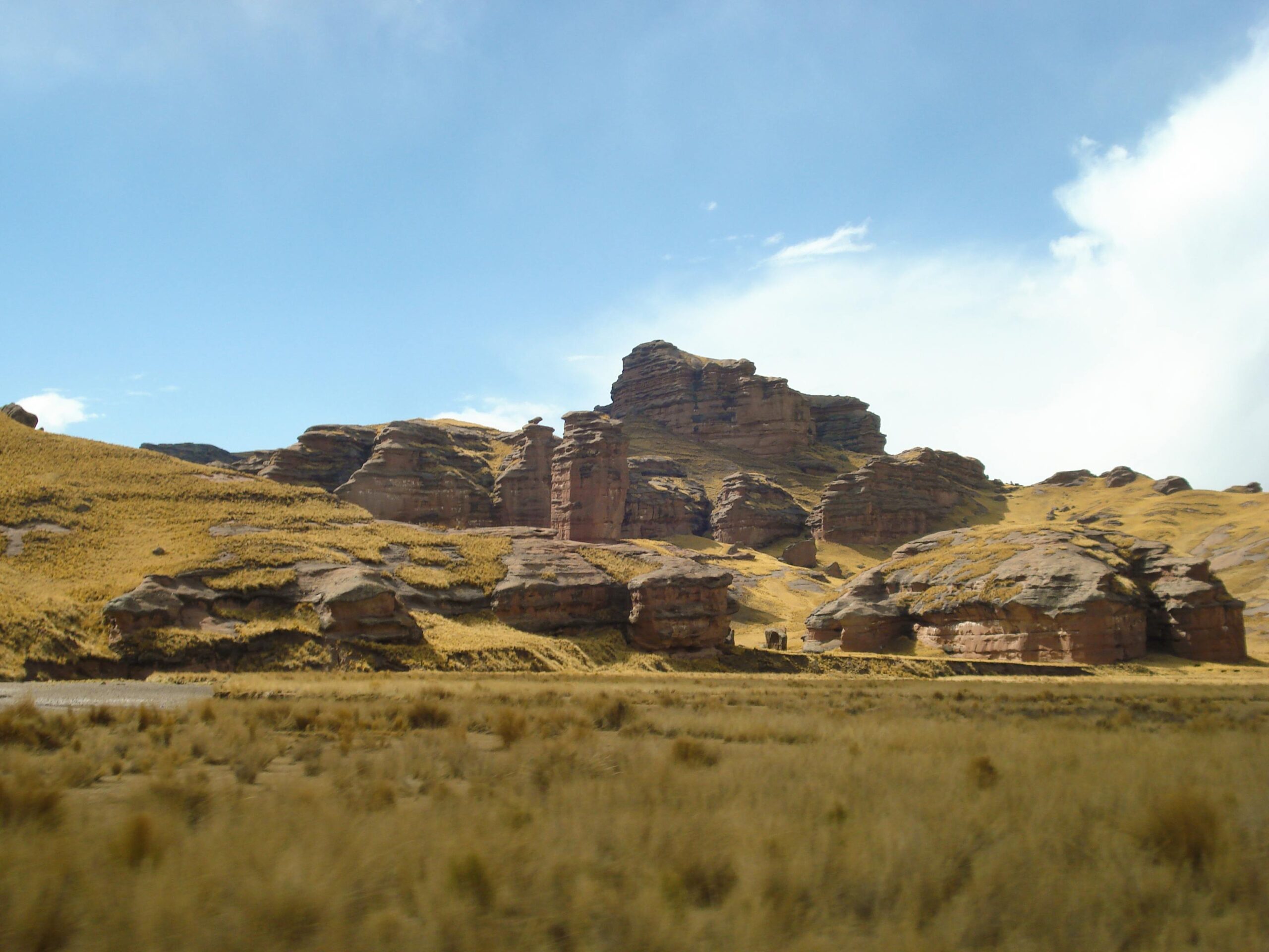 Layered rock formations in a grassy highland under a clear blue sky.