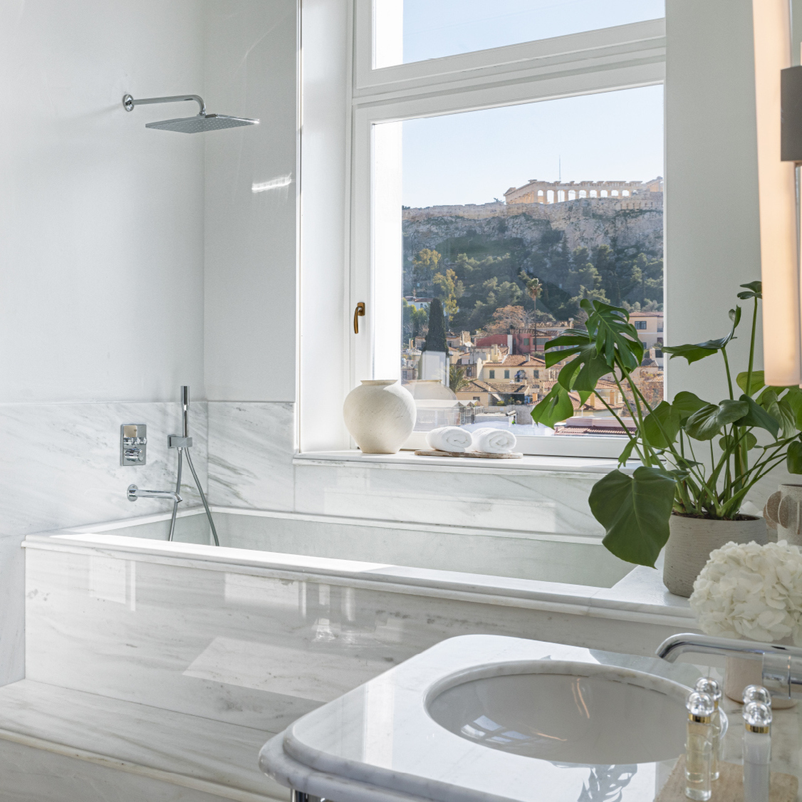 Stylish bathroom featuring a marble bathtub, a round sink, and a view of the Acropolis through large windows.