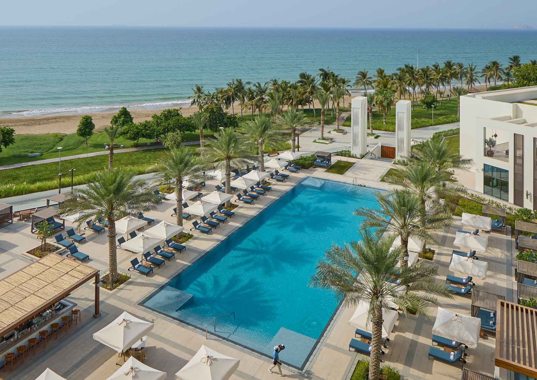 A view of Mandarin Oriental Muscat's pool, which is lined with palms and sun loungers.