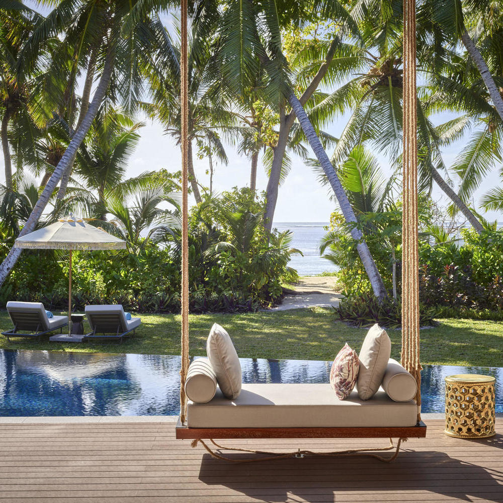 The outdoor area of a villa at Waldorf Astoria Seychelles Platte Island, featuring a pool, sun loungers in a garden and a path to the beach.