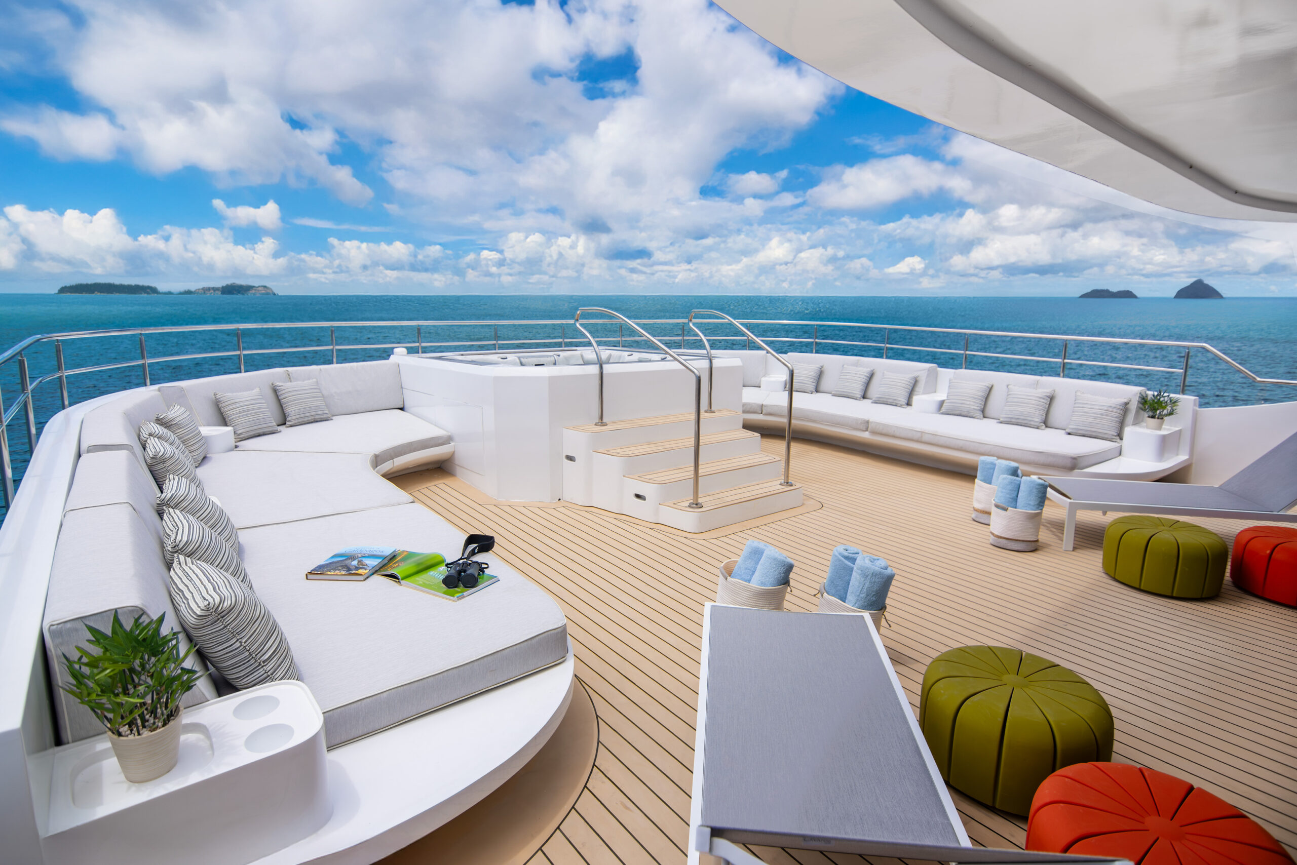 Open deck with lounge banquette around the edge and in the distance blue water and sky with clouds.
