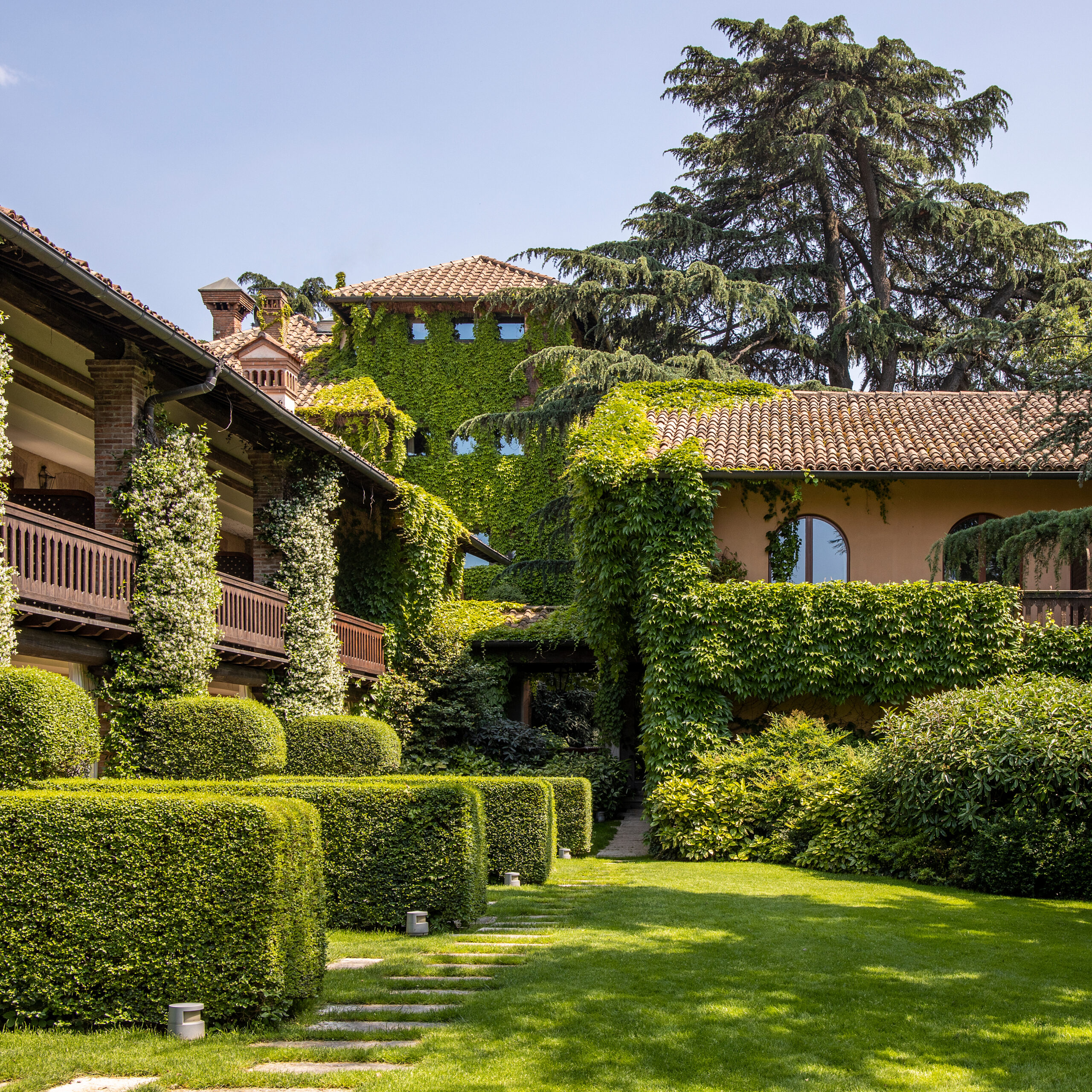 Exterior of a villa covered in ivy with lots of hedges and green lawns.