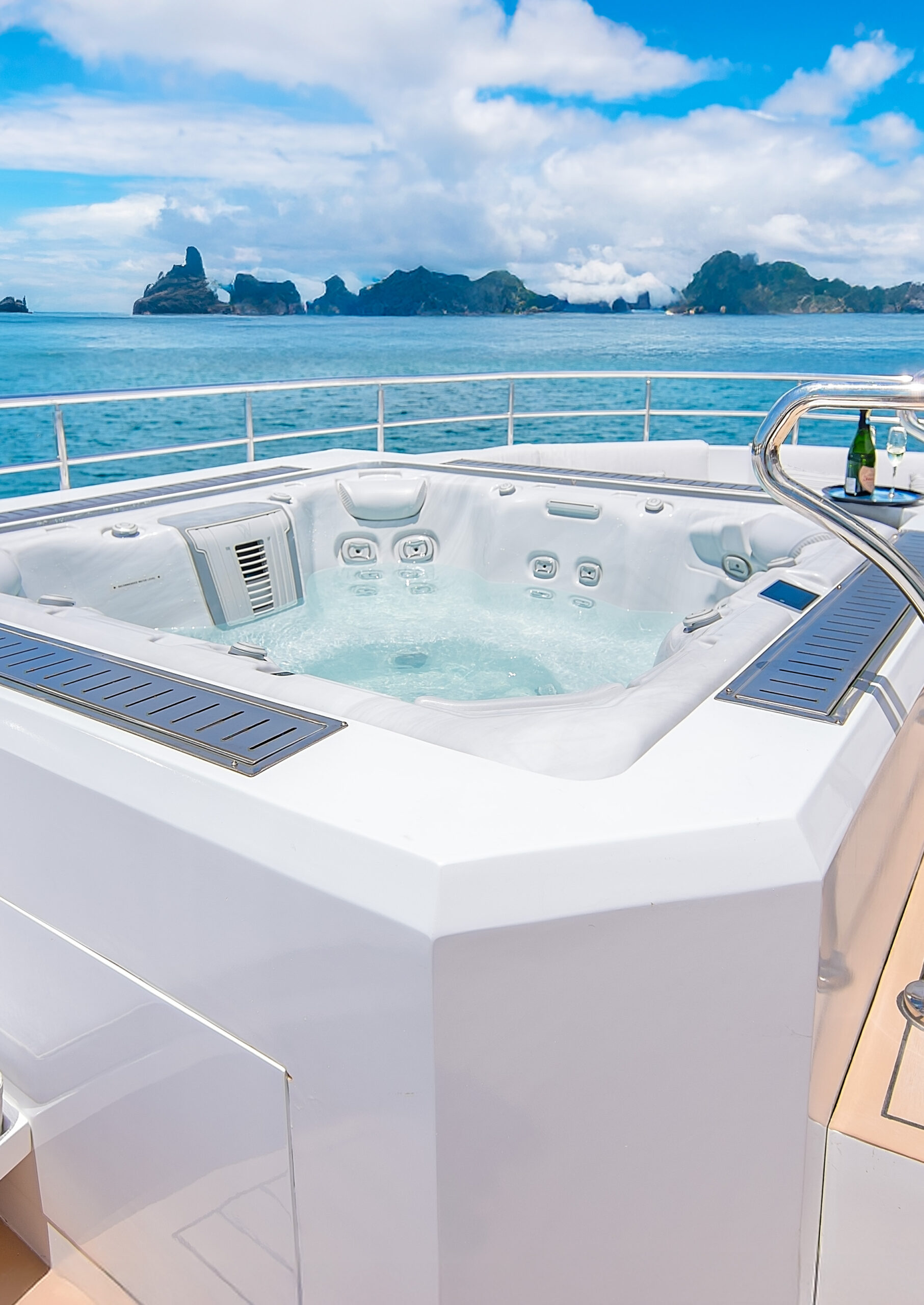 Hot tub on an open ship deck overlooking blue sea and mountains in the distance.