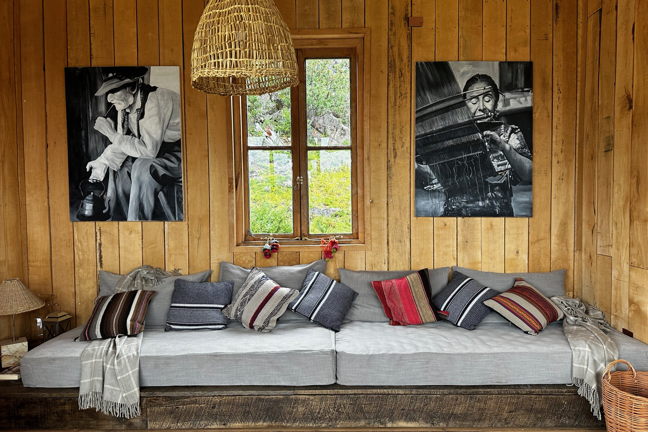Wood-panelled wall with two large black-and-white portrait photographs above a long, cushioned sofa decorated with striped and textured pillows.