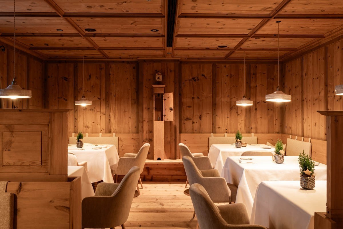 Restaurant interior with blonde wood walls and floors and a set of five tables with white table clothes, tan plush chairs and a lamp hanging over each.