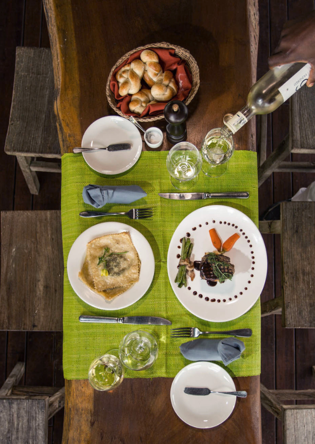 Overhead view of a table covered with a green cloth, wine glasses, two plates of food and a bread basket