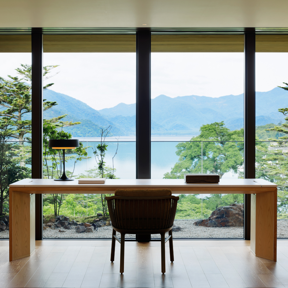 Minimalist desk facing floor-to-ceiling windows with view of lake and mountains
