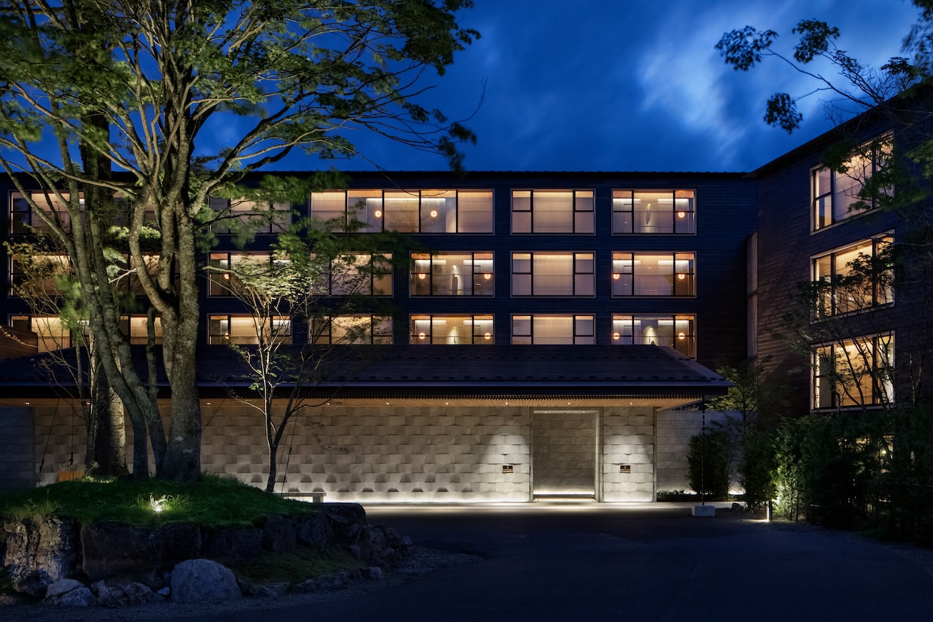 Exterior view of modern hotel at night with illuminated windows and a tree in the foreground