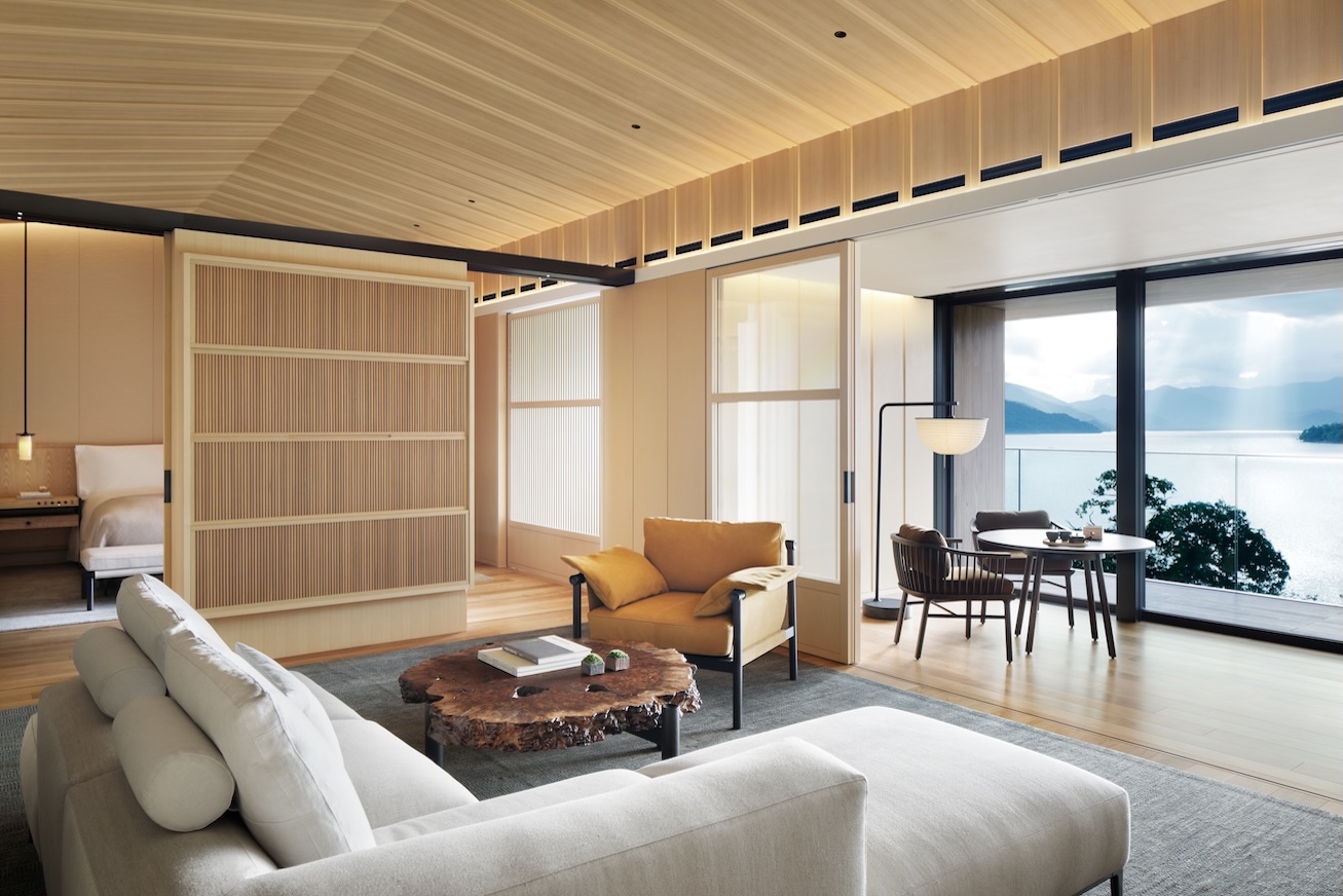 Modern hotel room with sofa, chair and large windows with view of a lake