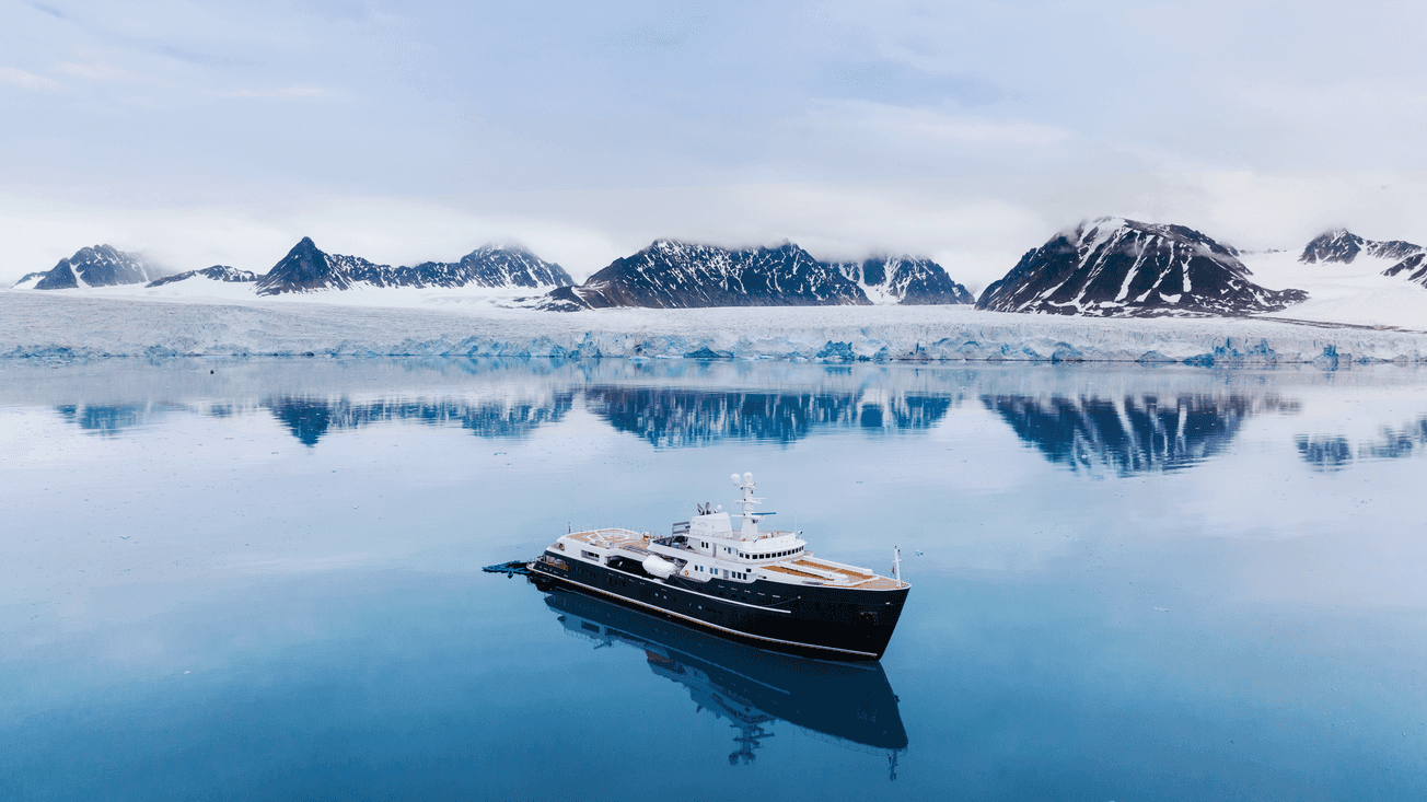 An aerial of Aqua Lares cruising across the water with snowy mountains in the background.