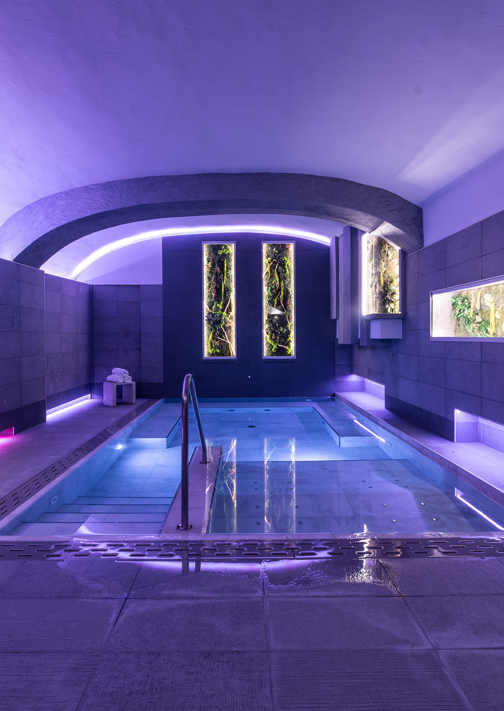 Indoor pool with purple lighting and two long windows at the back of the room.