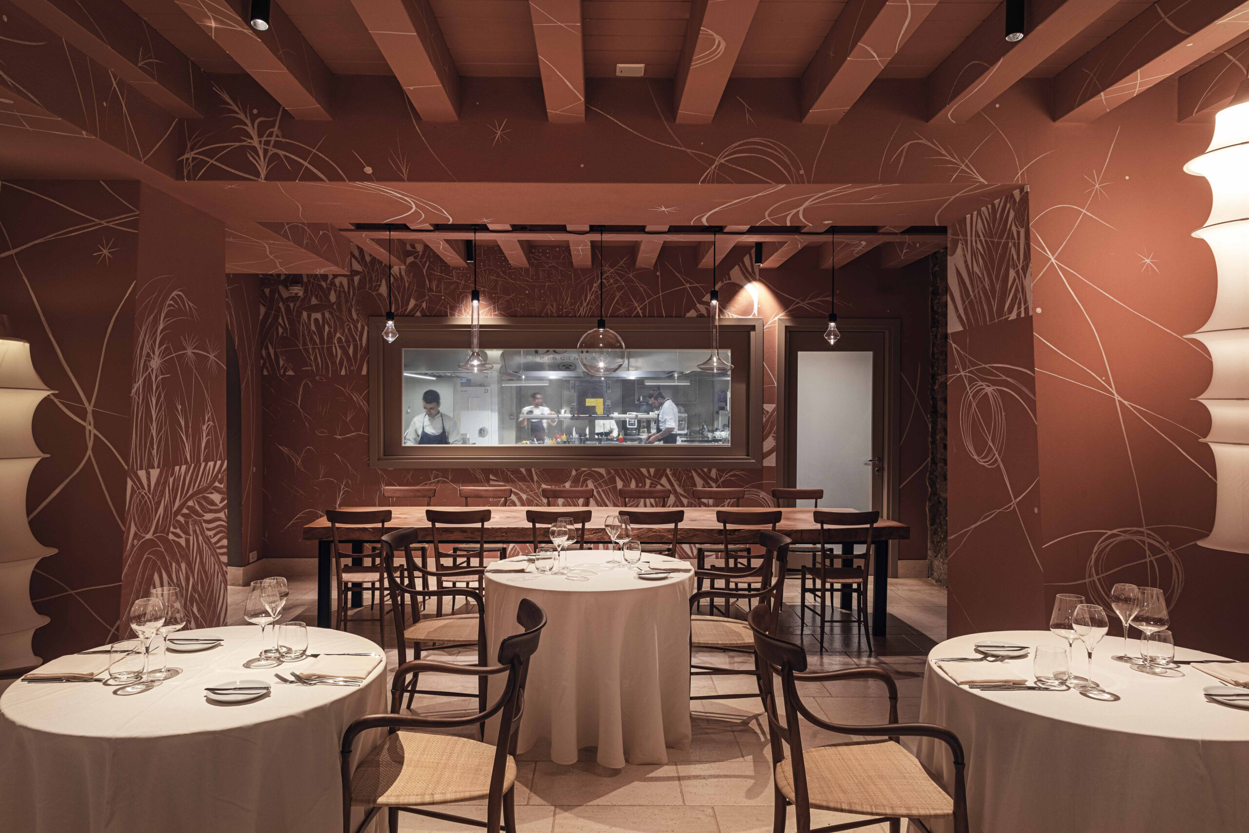 Interior view of the restaurant with muted tones and round tables with wrought-iron chairs.